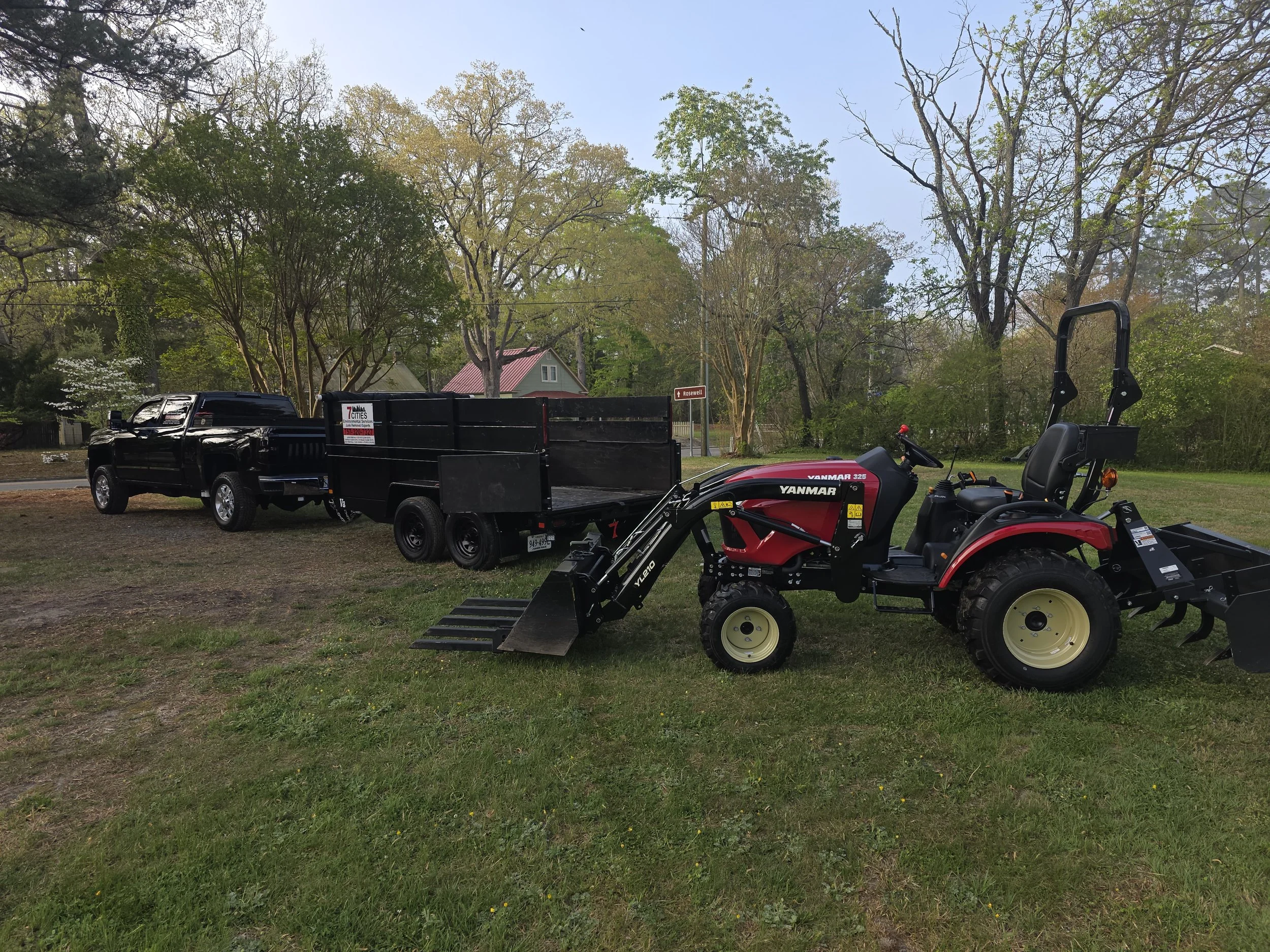 A yard scene with trees, a house with a red roof, a black pickup truck with a trailer, a red Yanmar tractor, and a small sign indicating the street name Rosewell.
