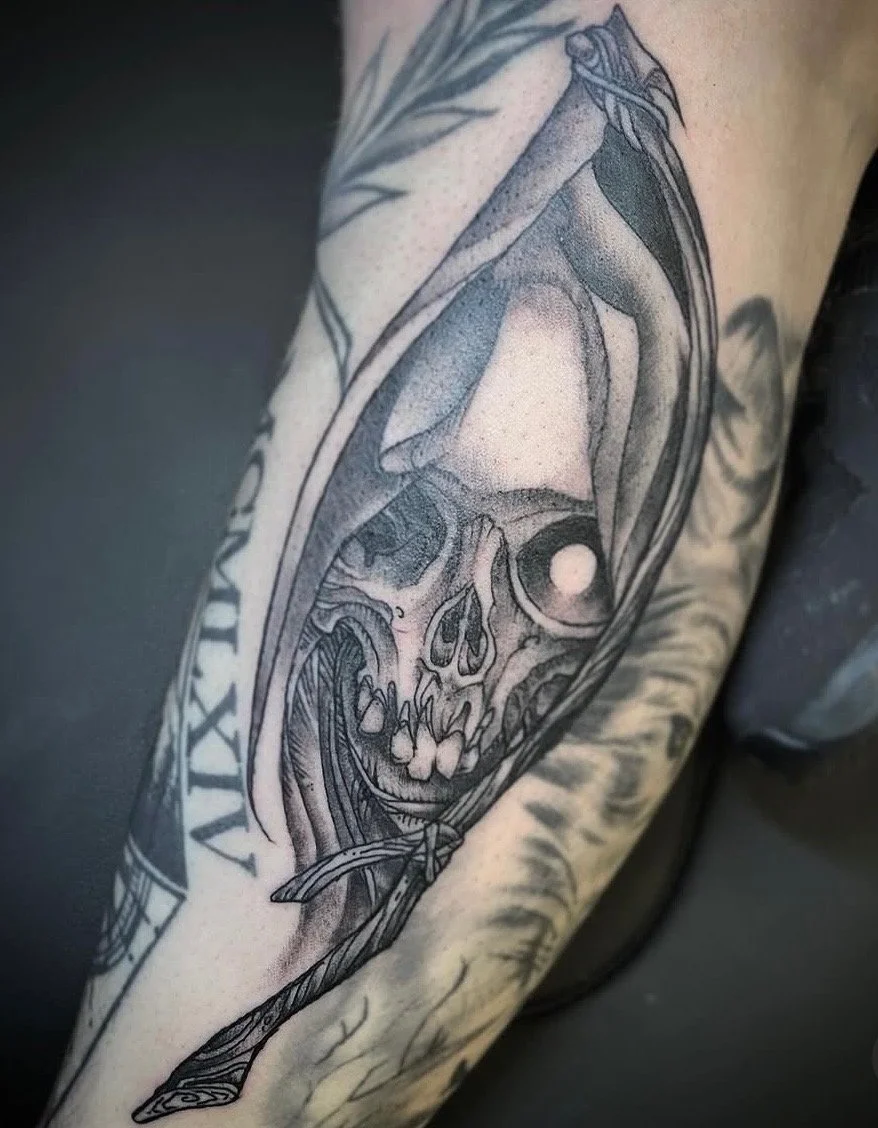 Black and gray tattoo of a human skull with detailed shading, wrapped in a large dagger or sword on a person's arm.