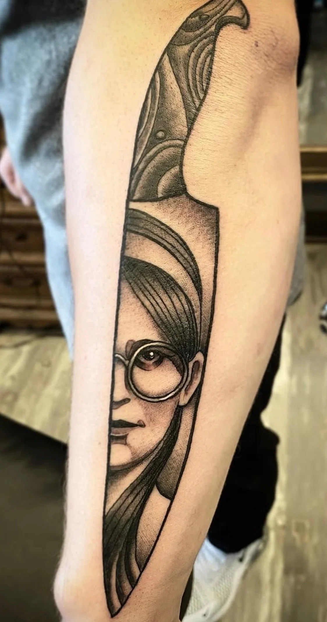 Tattoo of a woman's face with a circular earring, showcasing stylized hair and facial features, on a person's upper arm.