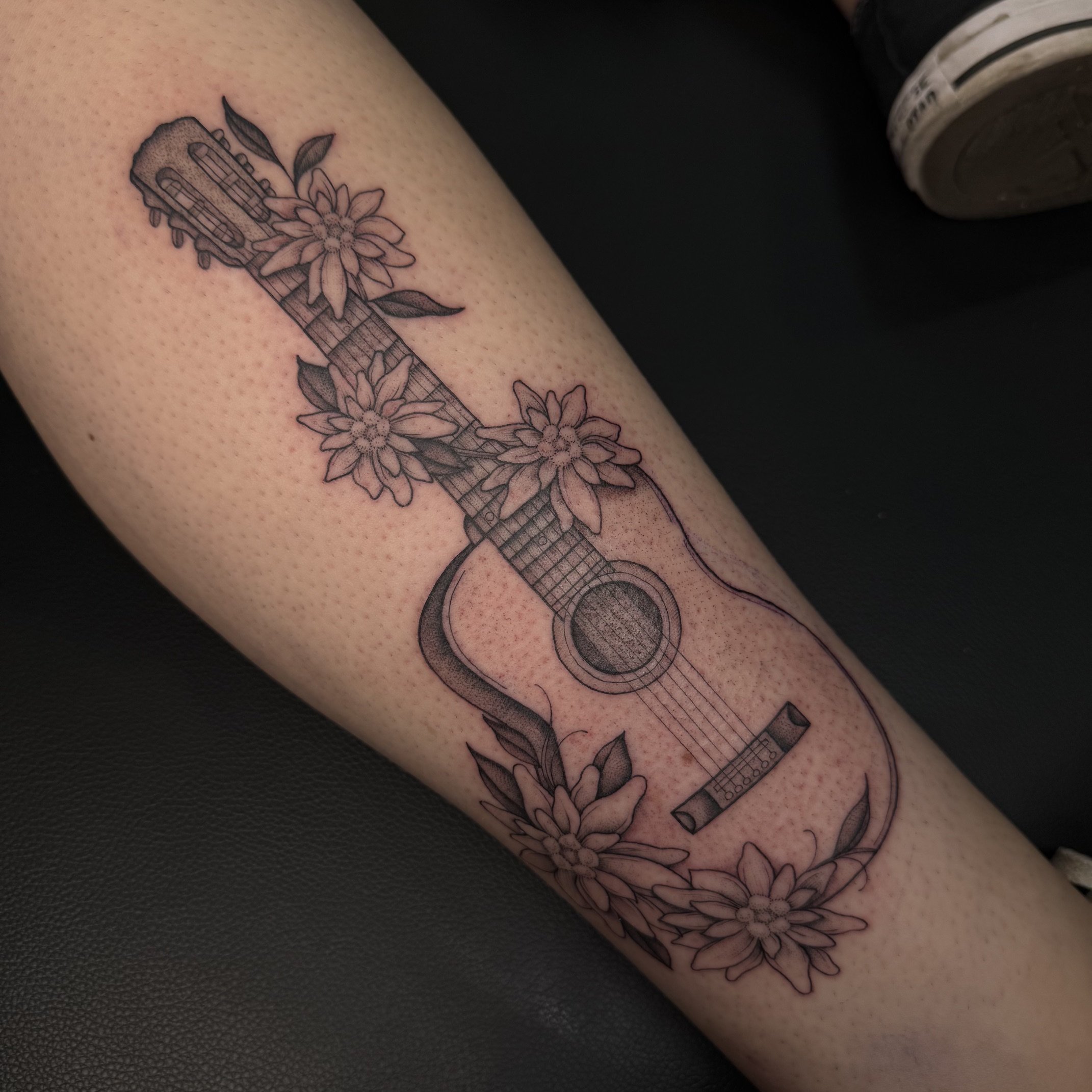 Tattoo of a guitar with flowers on a person's arm.