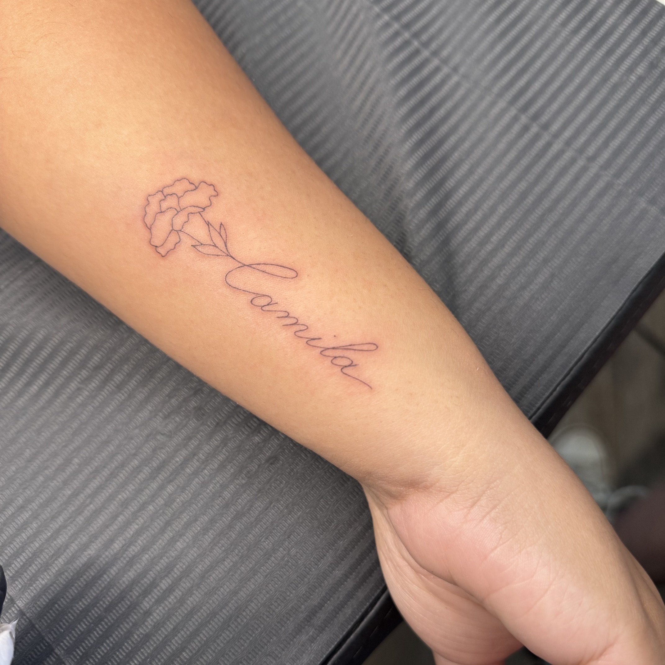 A person's arm with a delicate line drawing of a flower tattoo and the word "family" written in cursive.