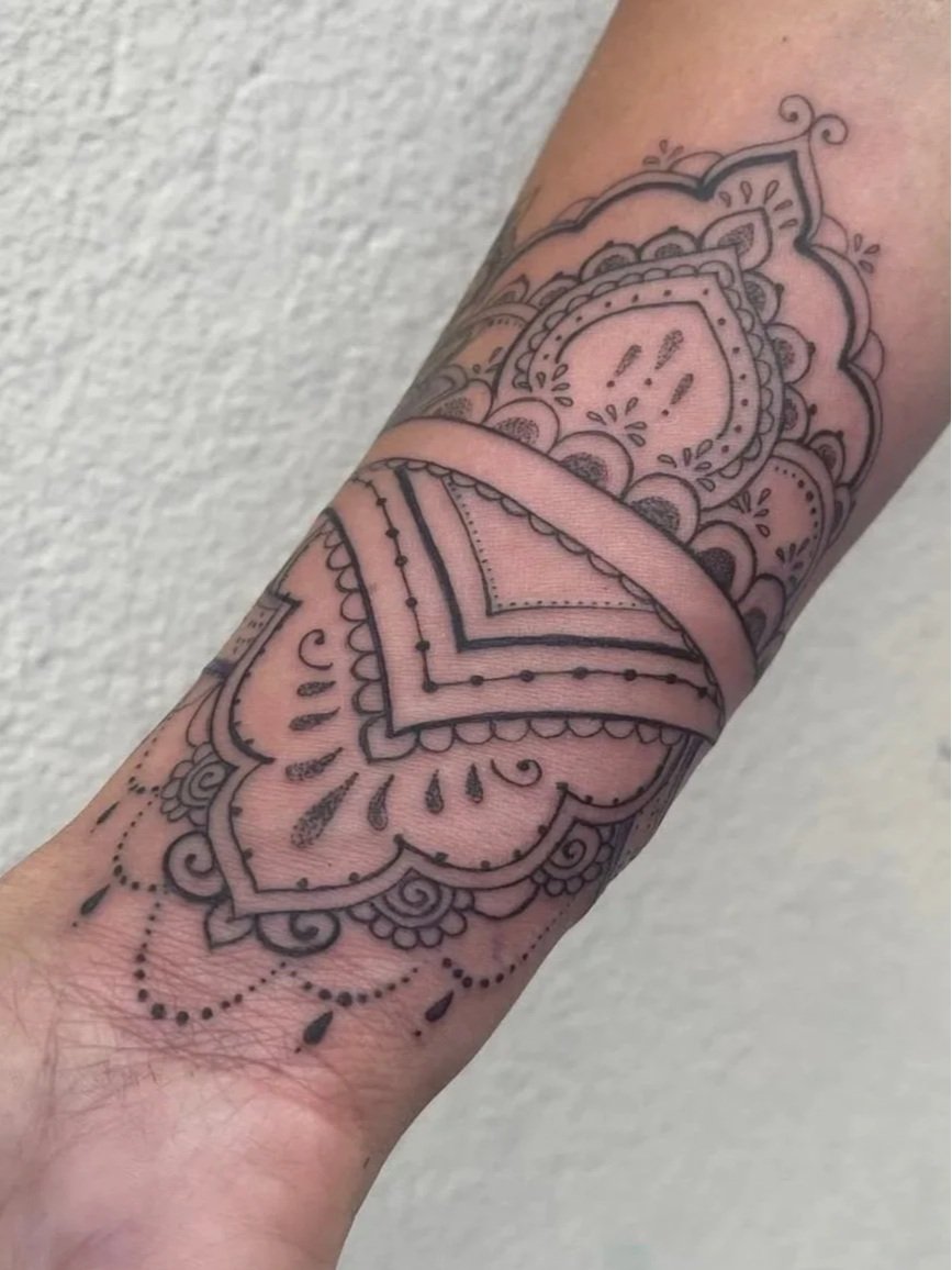 Close-up of a person's forearm with a detailed black outline henna or tattoo style design featuring floral and geometric patterns by Kelly Cunningham.
