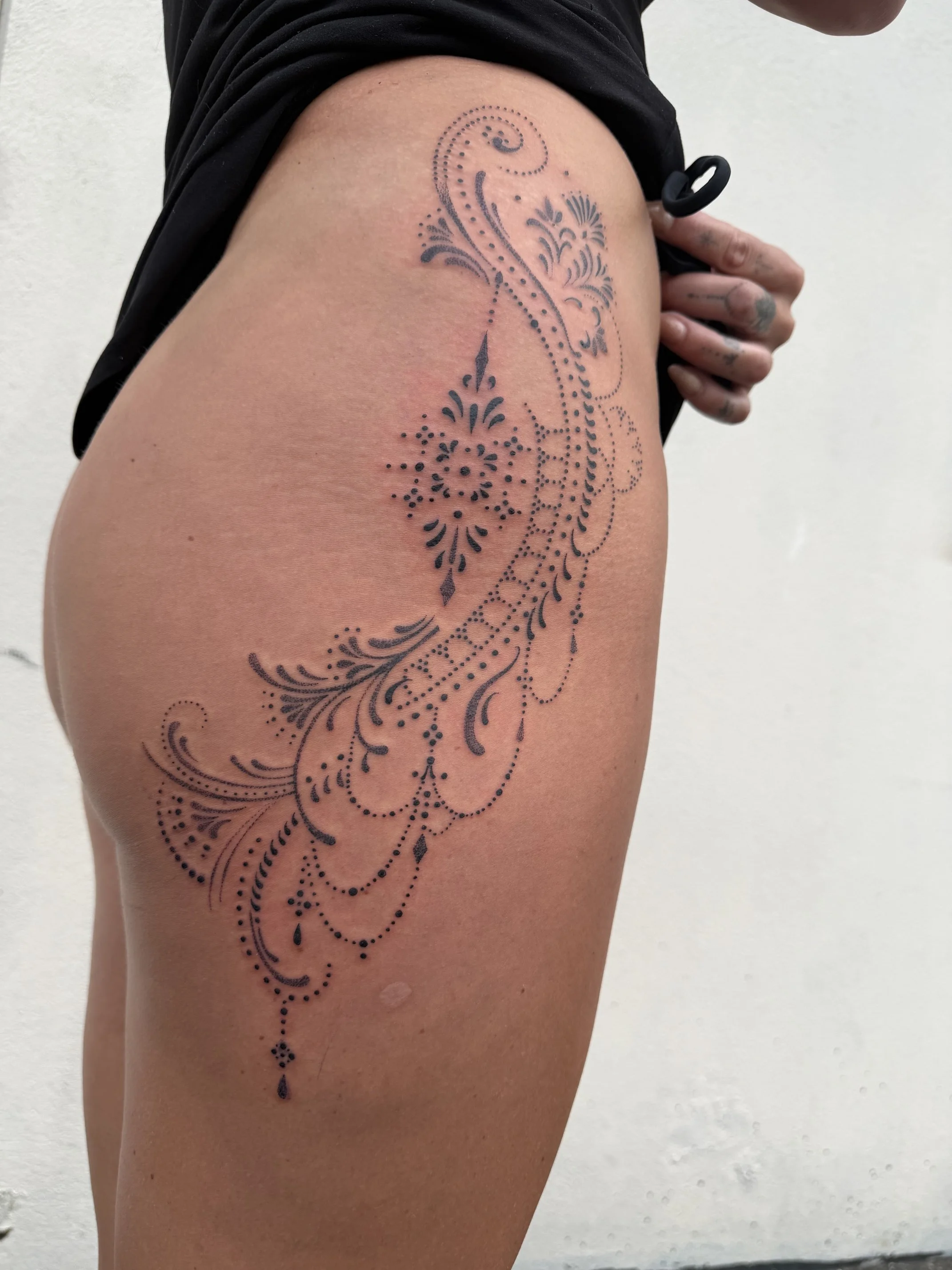 Ornamental blackwork tattoo by Kelly Cunningham featuring intricate floral motifs, decorative dotwork, and flowing henna-inspired patterns from the hip to the upper thigh.
