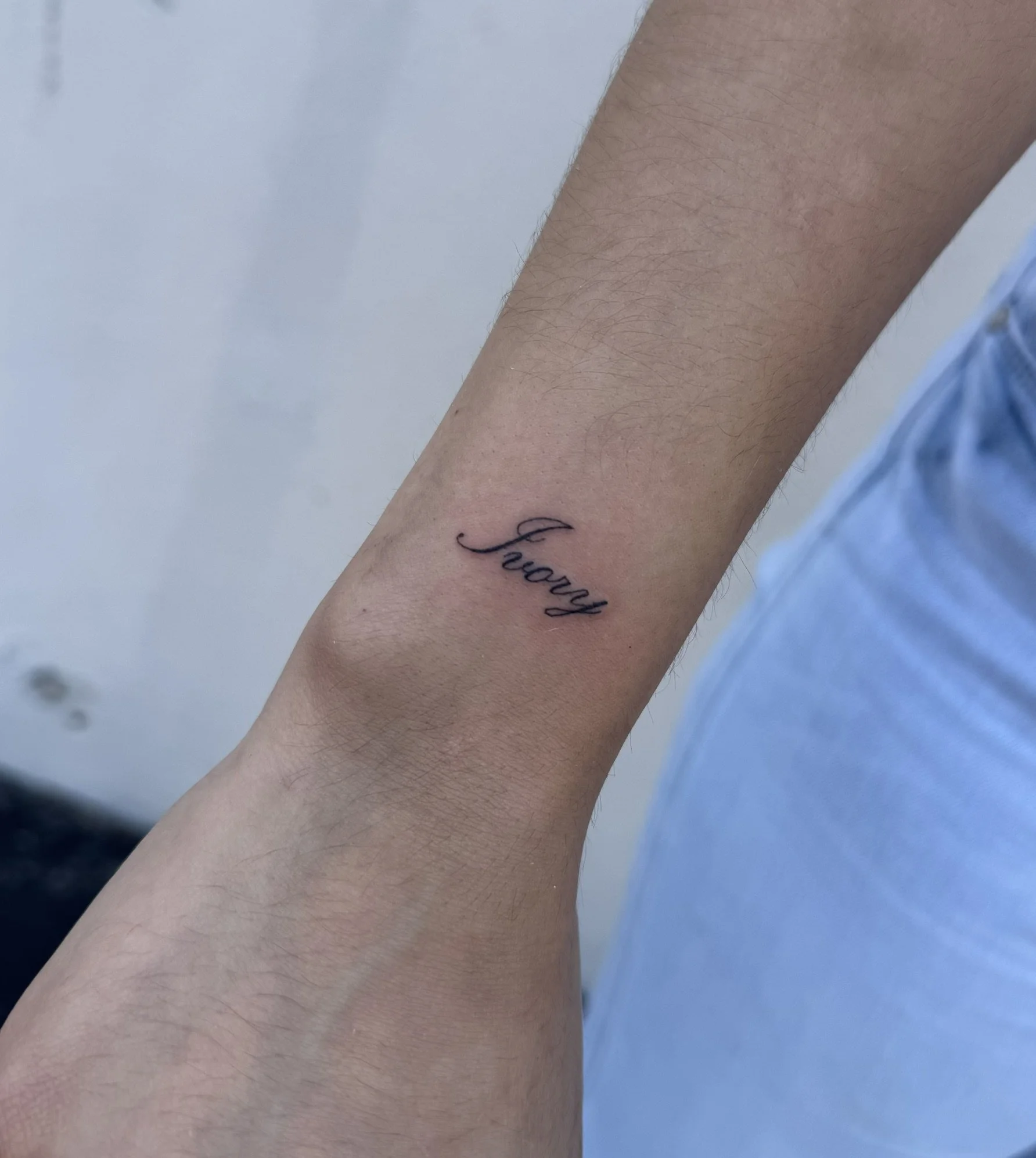 Close-up of a person's arm with a small tattoo that says 'laugh' in cursive.