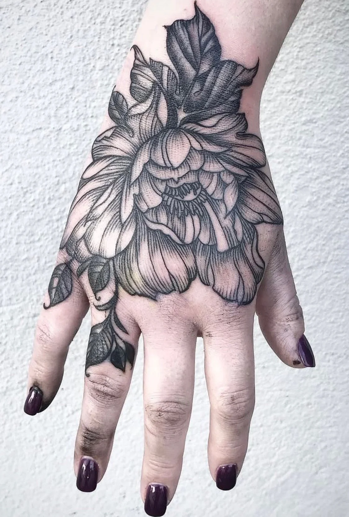 Black and gray floral tattoo on the top of a person's hand and wrist.