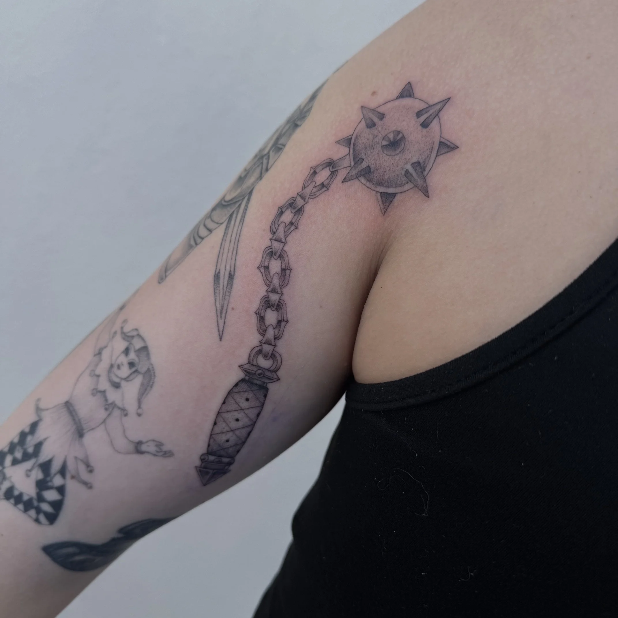 Close-up of a tattoo on a person's arm featuring a spiked circular design connected to a chain.