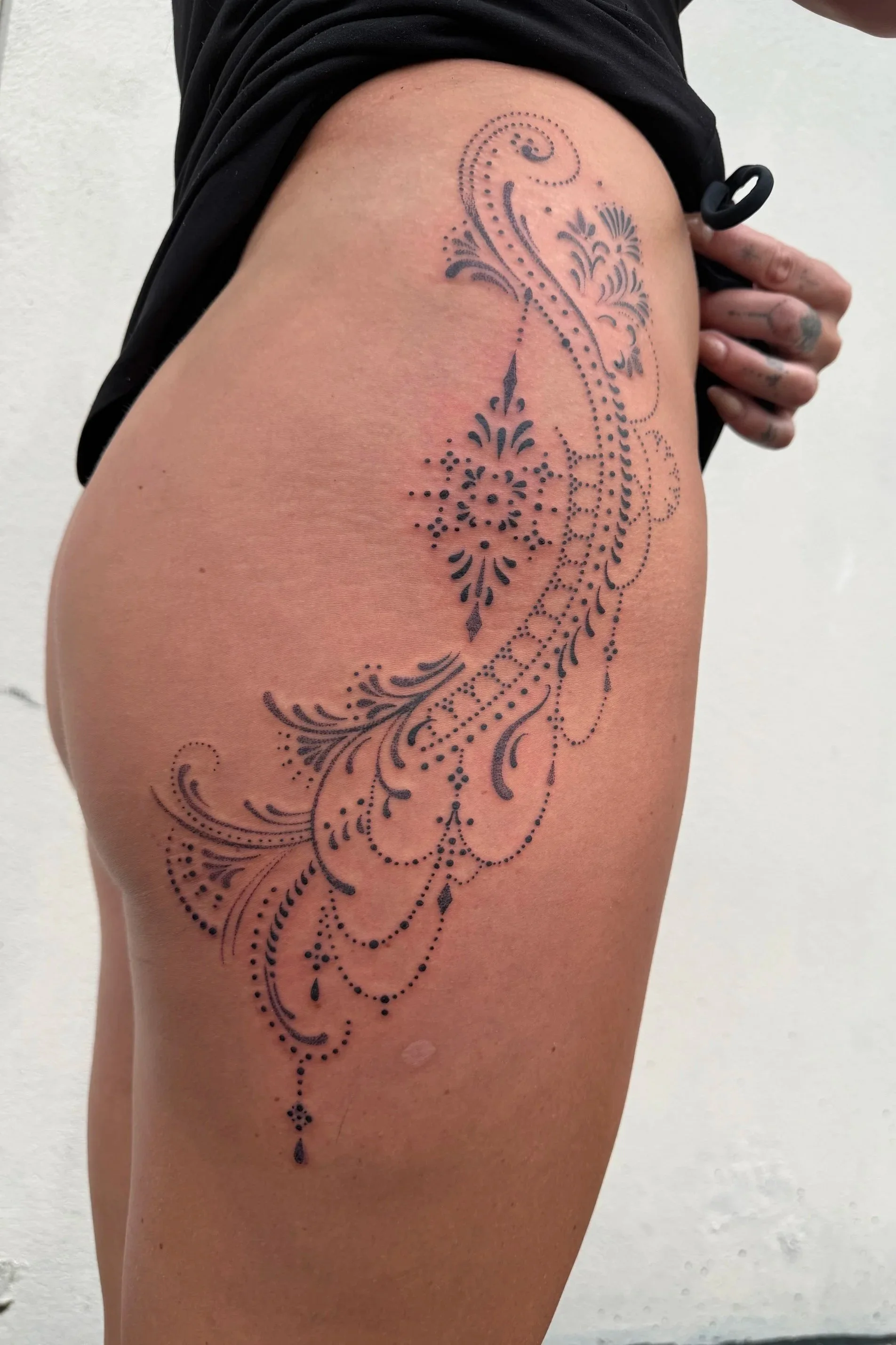 Ornamental blackwork tattoo by Kelly Cunningham featuring intricate floral motifs, decorative dotwork, and flowing henna-inspired patterns from the hip to the upper thigh.