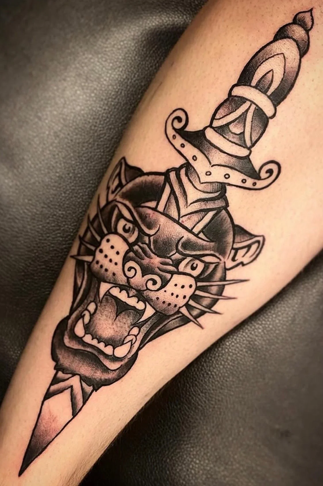 Tattoo of a fierce panther with an open mouth, sharp teeth, and a dagger passing through its head.