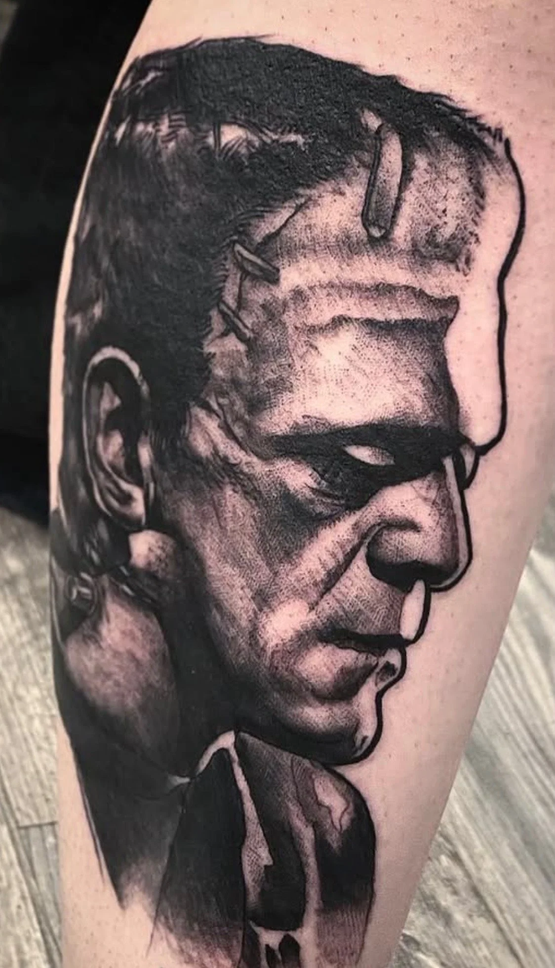 Black and gray ink tattoo of a man's face in profile, with bold outlines and shading, on a person's arm.