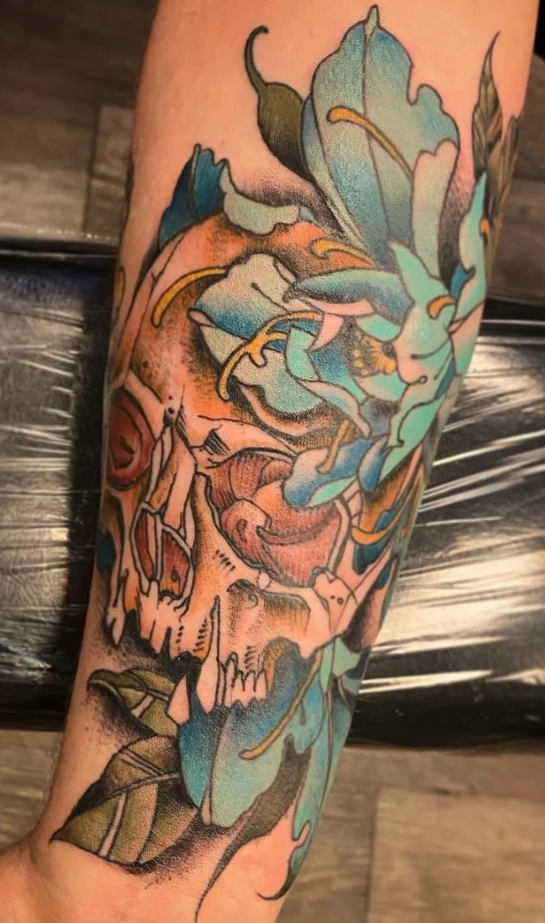 Tattoo art on a person's arm featuring a colorful and stylized human skull intertwined with floral and abstract designs.