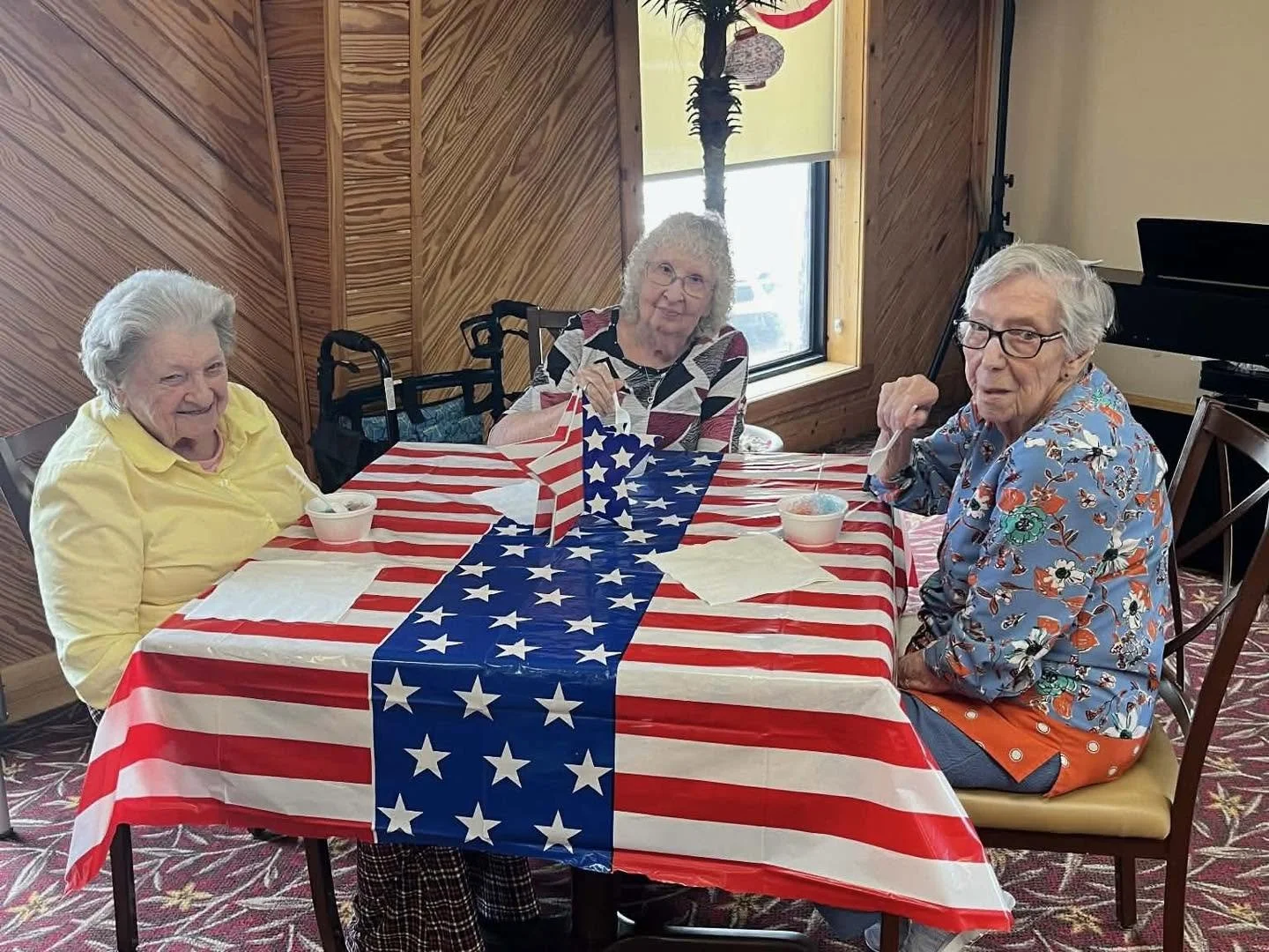 Three elderly women sitting at a table celebrating with American flag-themed decorations and food.