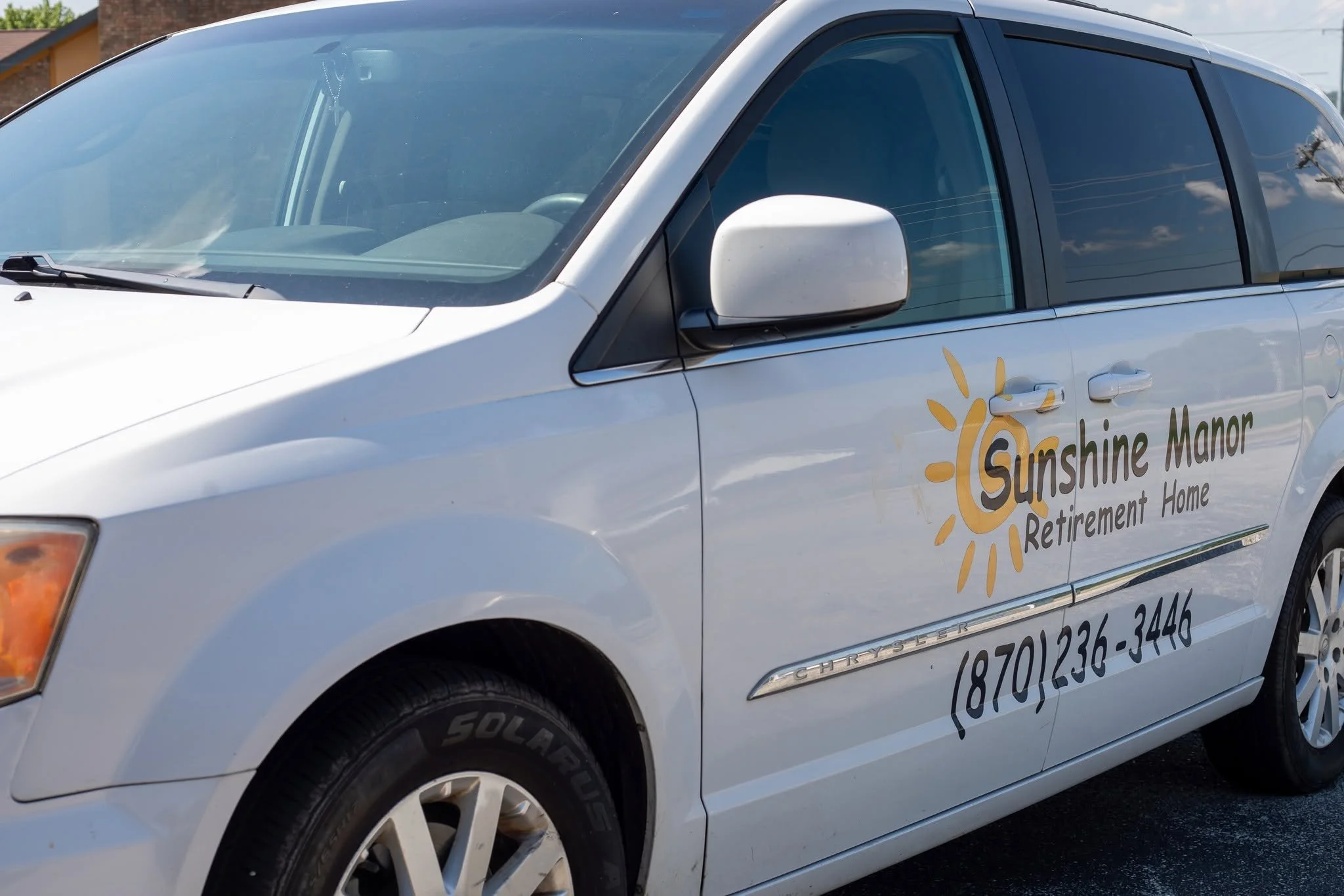 A white vehicle with logo and contact information for Sunshine Manor Retirement Home on its side.