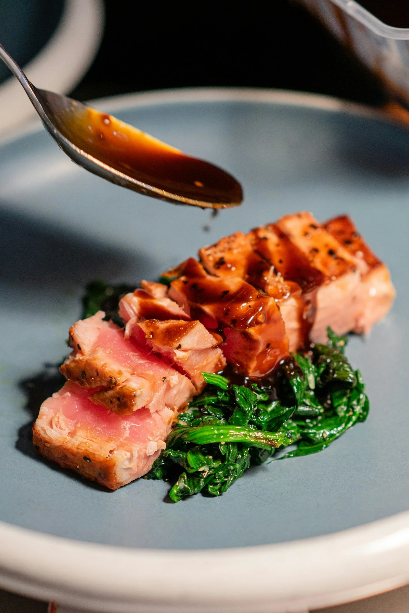 A plated dish with sliced grilled salmon, sautéed spinach, and a piece of seared tuna topped with sauce.