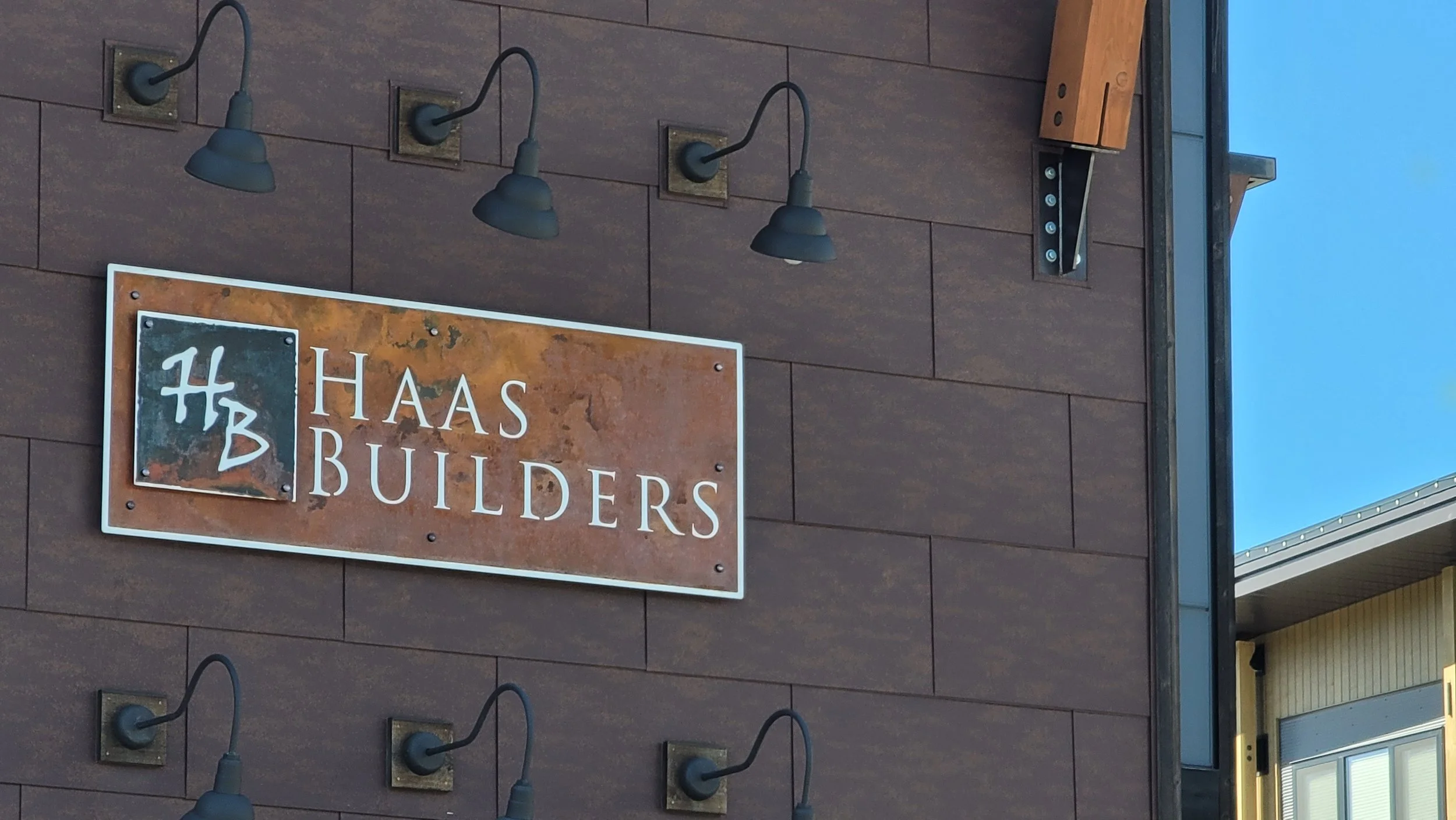 Exterior of a building with a sign that reads 'Haas Builders' and four black outdoor wall-mounted lights above the sign.