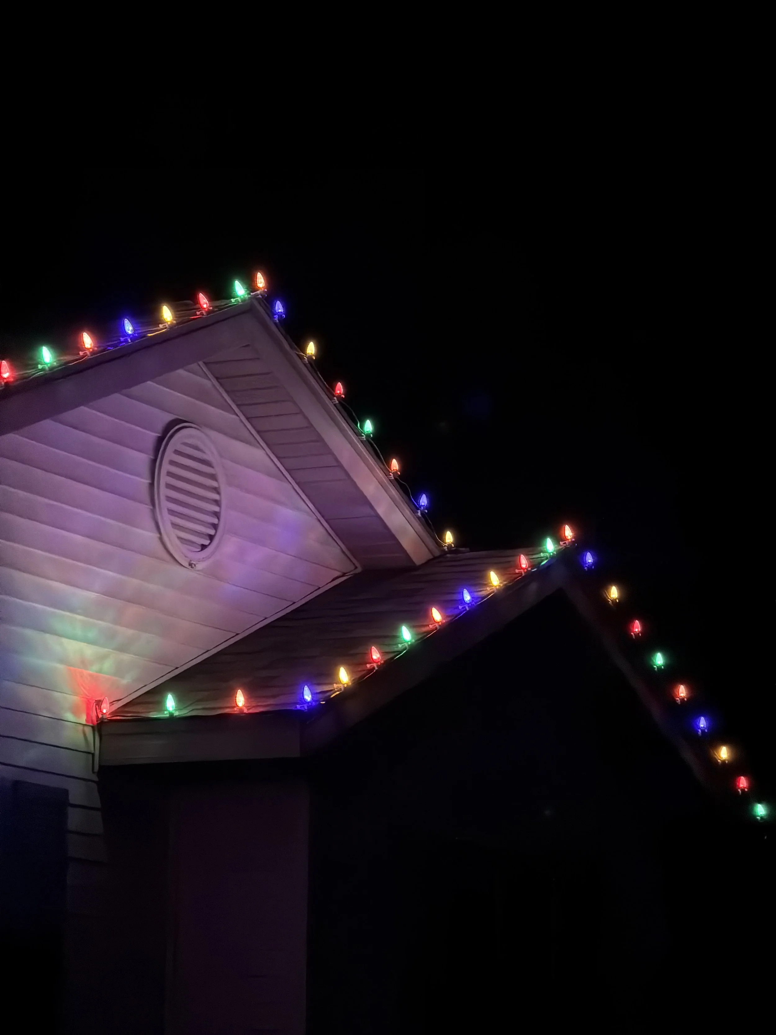 Colorful Christmas lights hanging on the roof of a house at night.