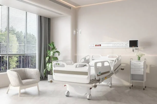 Empty hospital room with a bed, a chair, a potted plant, and medical equipment near a window with blinds.