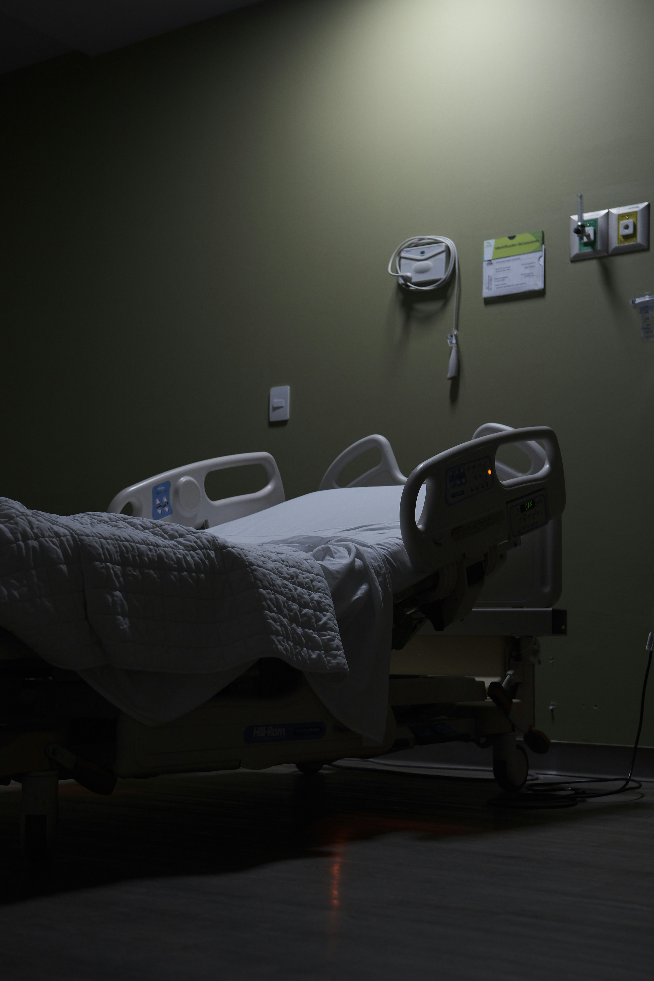 Empty hospital bed in a dimly lit room with medical equipment on the wall.