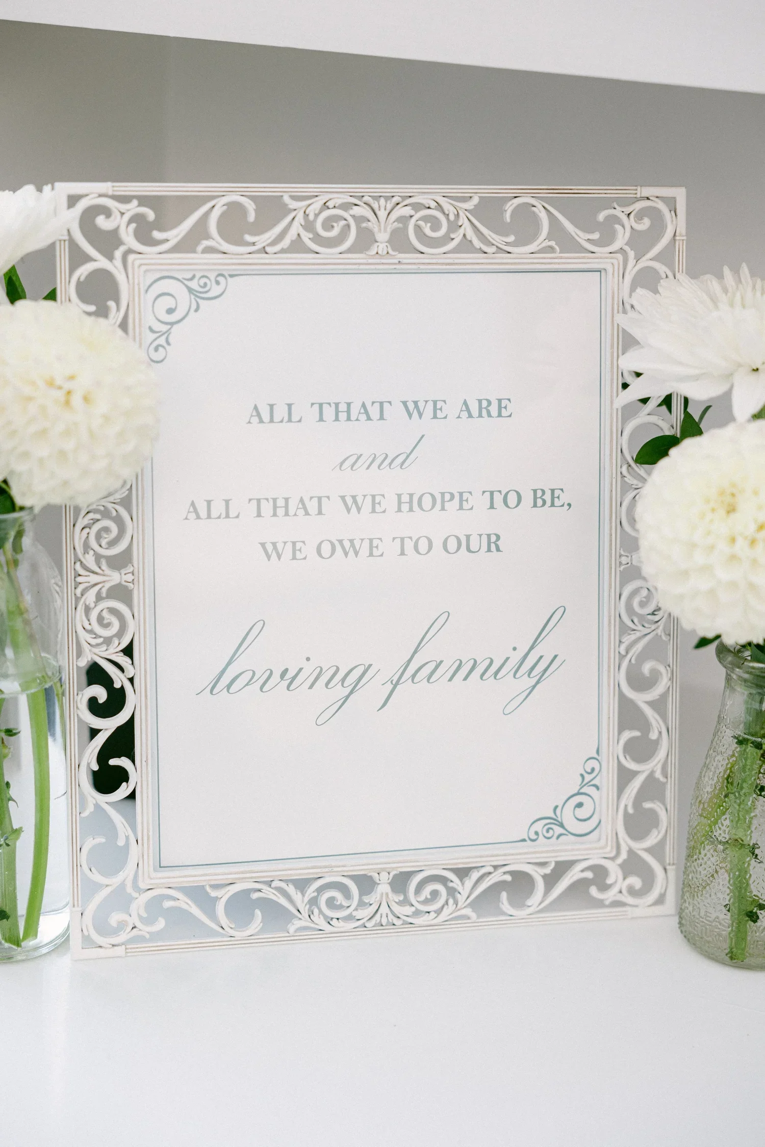 A decorative white frame with an inspirational quote about family, surrounded by white flowers in glass vases.