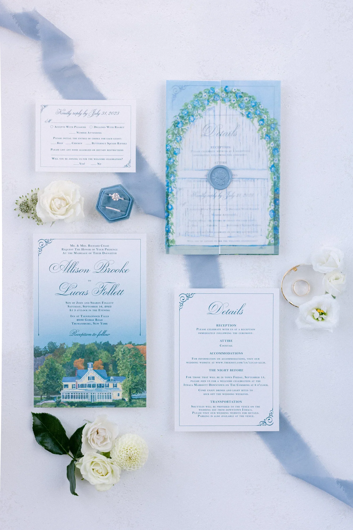 Wedding invitation and RSVP cards decorated with white flowers, green leaves, and a light blue ribbon on a white surface.