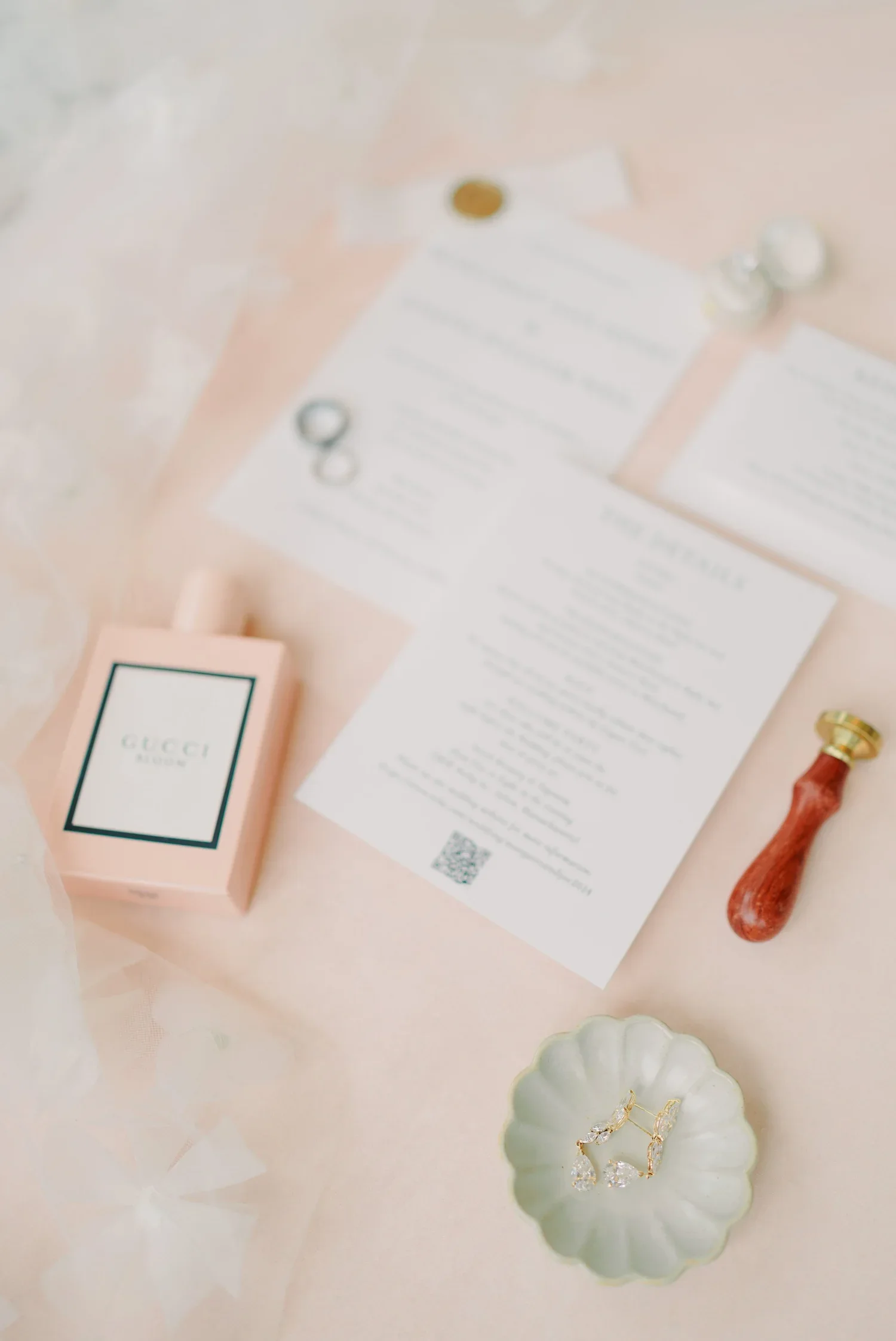 Flat lay of jewelry, a Gucci perfume box, papers, and decorative items on a pink surface.