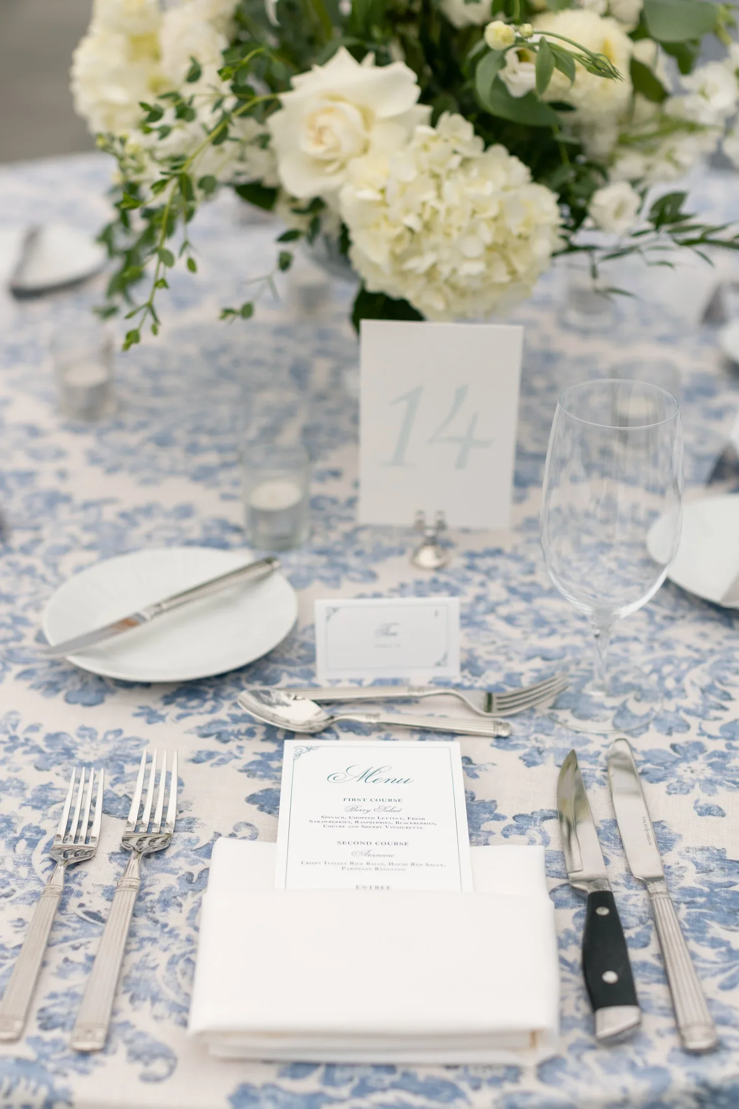 Elegant table setting with silverware, wine glass, menu, floral centerpiece, and table number 14 at a formal event.