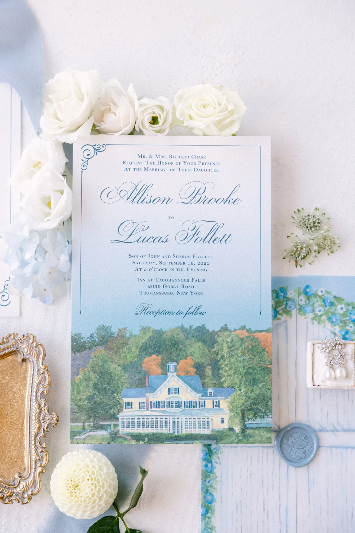 Wedding invitation with white flowers, a gold-framed mirror, and a planting seed wax seal.