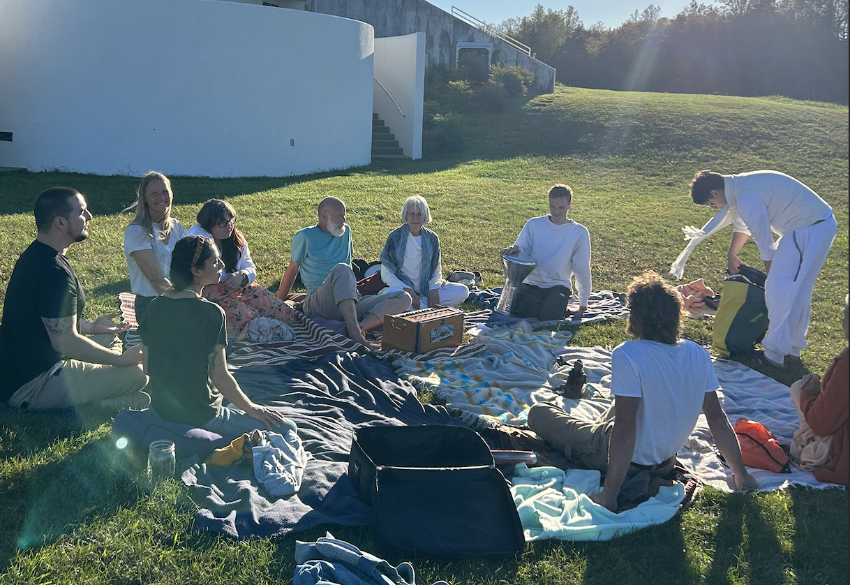 A group of people having a picnic outdoors on a sunny day, sitting on blankets on the grass in front of a white building.