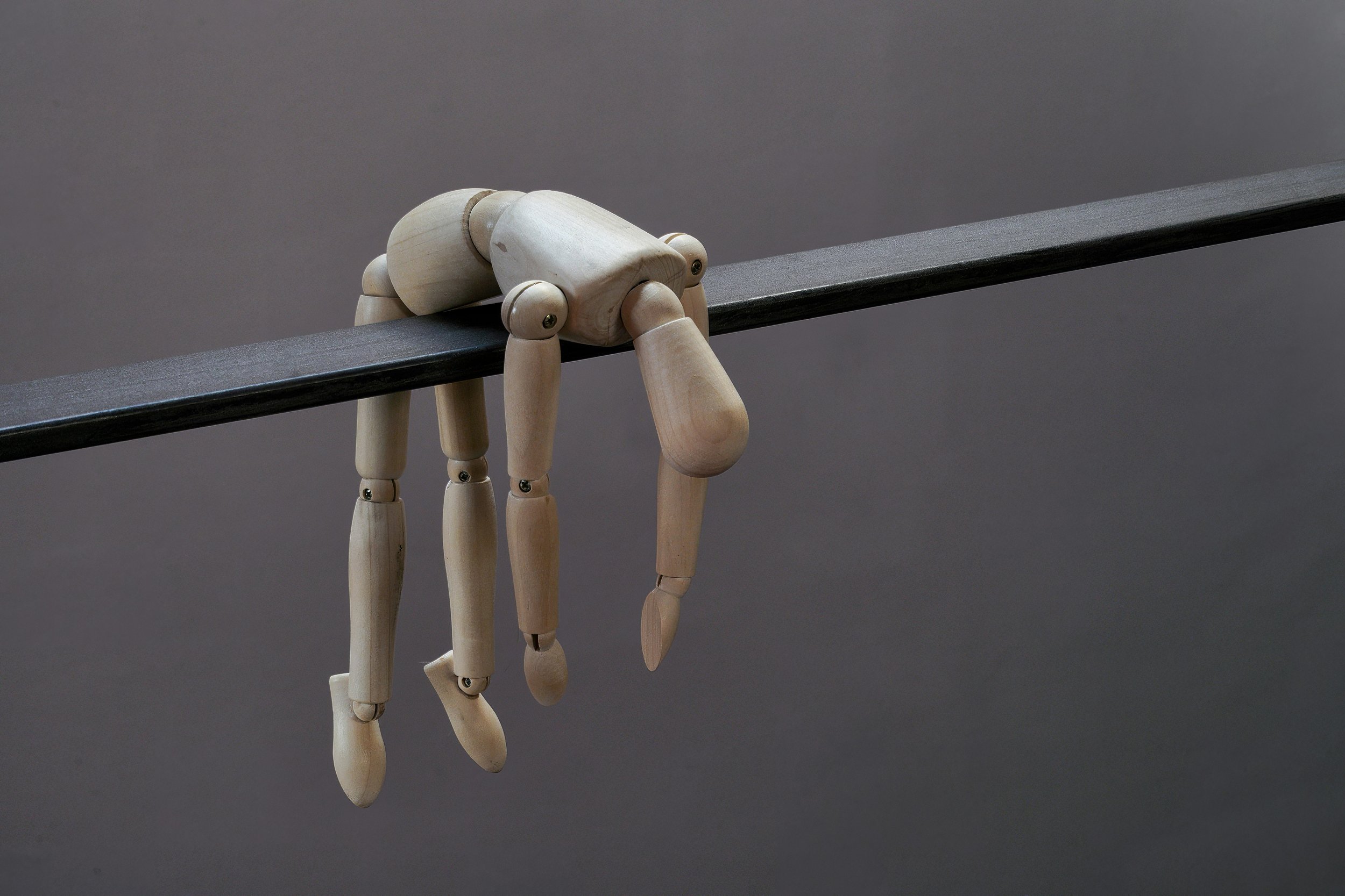 A wooden mannequin bending over and hanging off the edge of a black shelf or table.