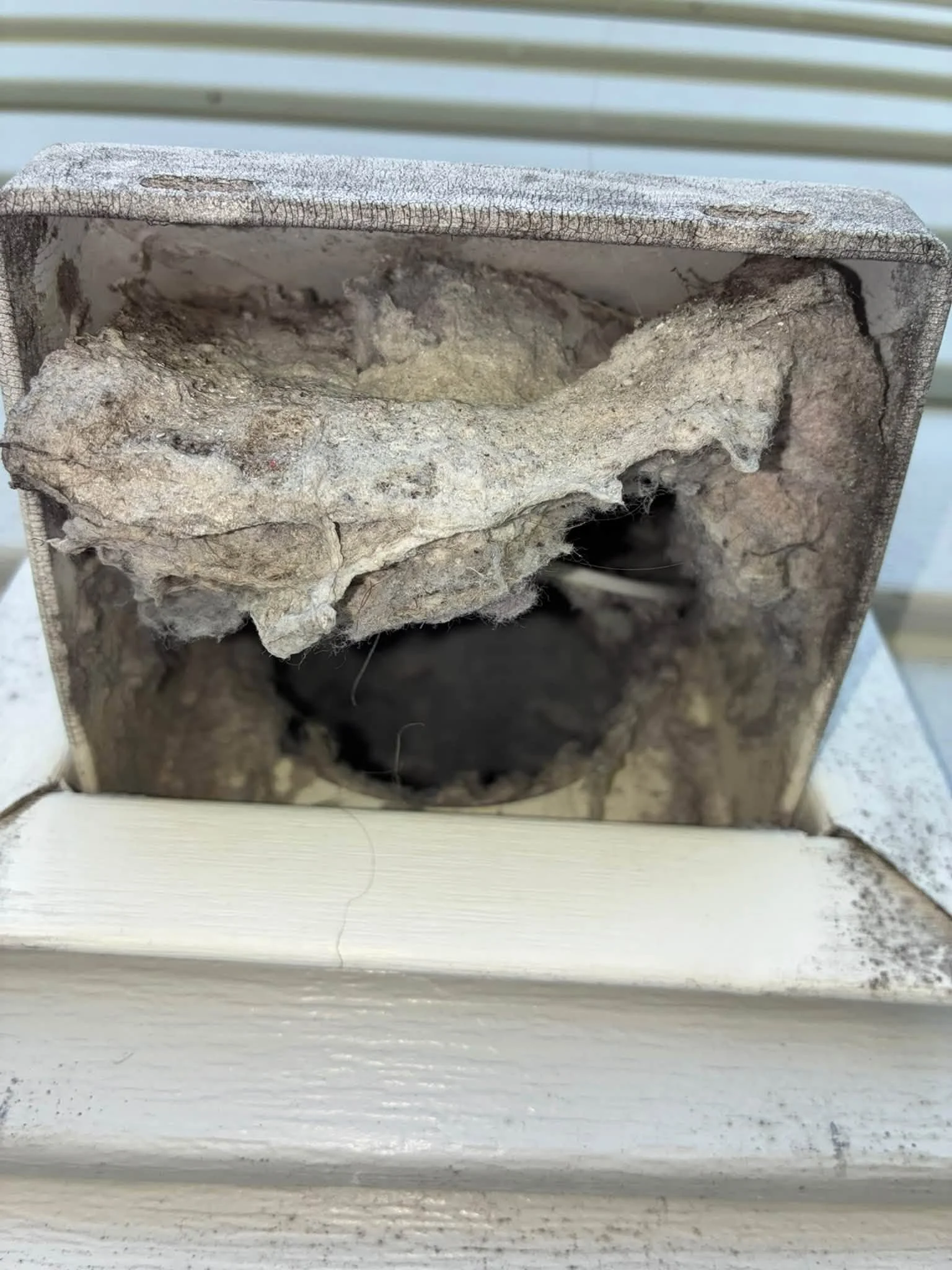 A close-up of a hollow section of a brick wall with rough, uneven surface and some debris inside, seen from above with white wooden siding at the bottom.