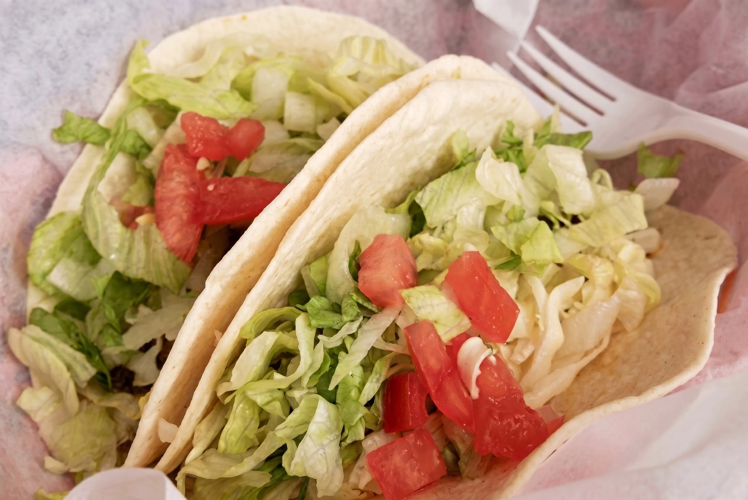 Close-up of two tacos filled with chopped lettuce, diced tomatoes, and shredded cheese in soft taco shells