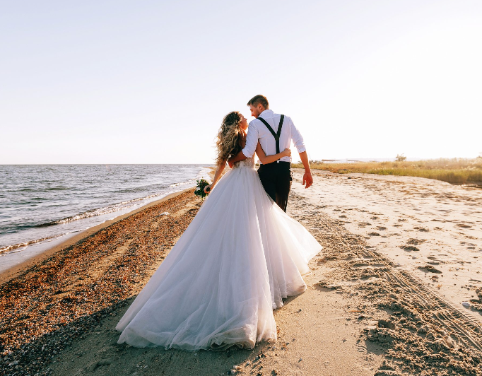 Bride and groom walking on a beach at sunset, holding each other