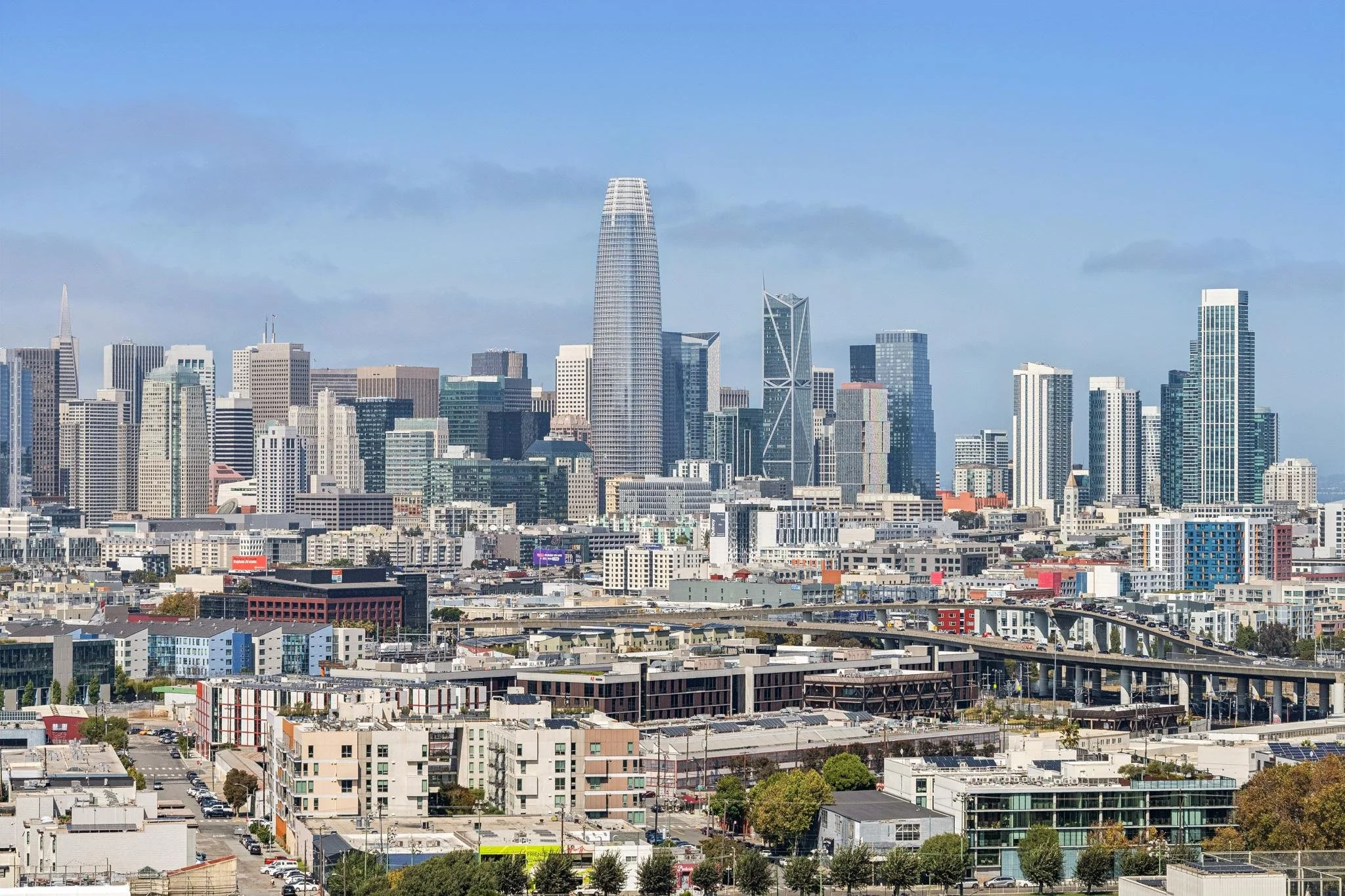 City skyline featuring a variety of high-rise buildings and skyscrapers, with a tall, rounded building prominently in the center, under a clear blue sky.