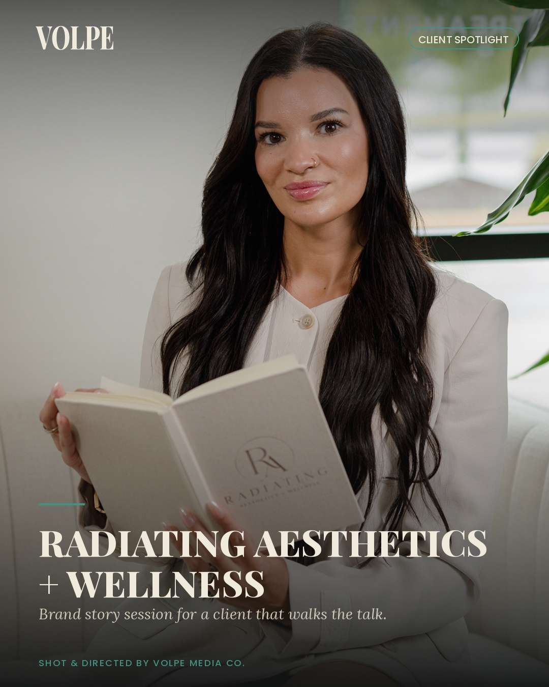 A woman with long dark hair holding an open book titled "Radiating Aesthetics" in a bright room with a window and green plant in the background.