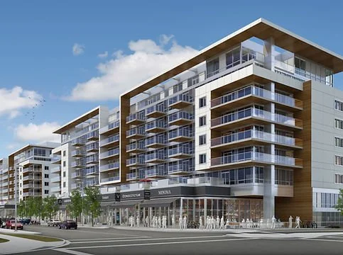 Modern multi-story residential and commercial buildings with glass balconies, retail shops on the ground floor, and a wide street with cars and pedestrians in an urban setting.
