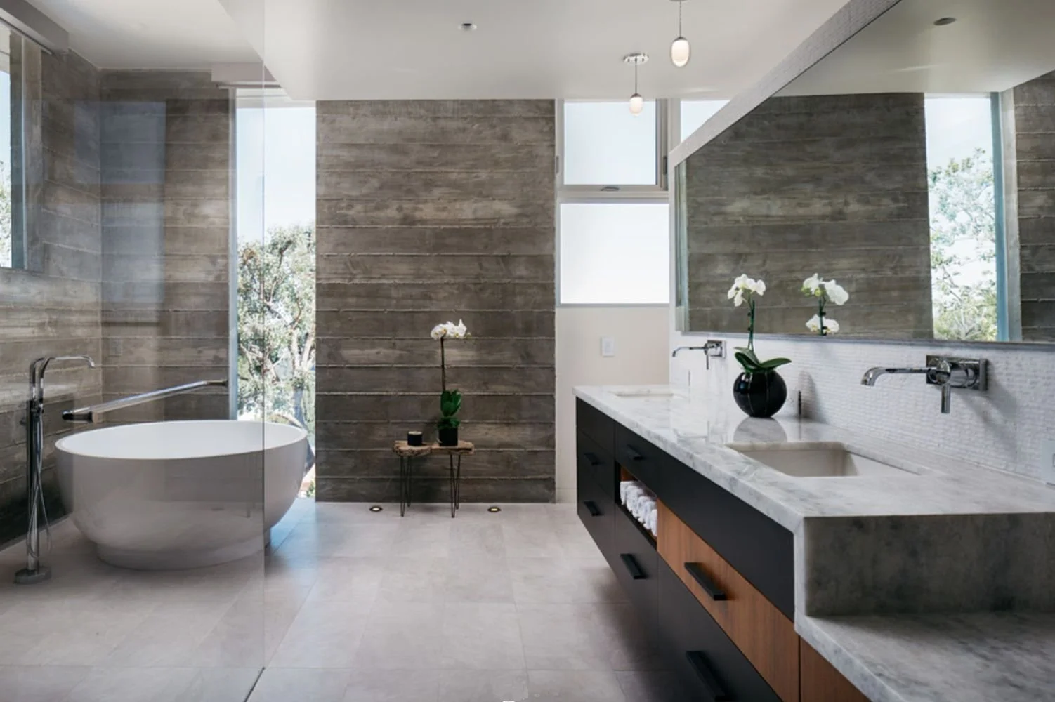 Modern bathroom with bathtub, large mirror, and vanity with sink and orchid plants.