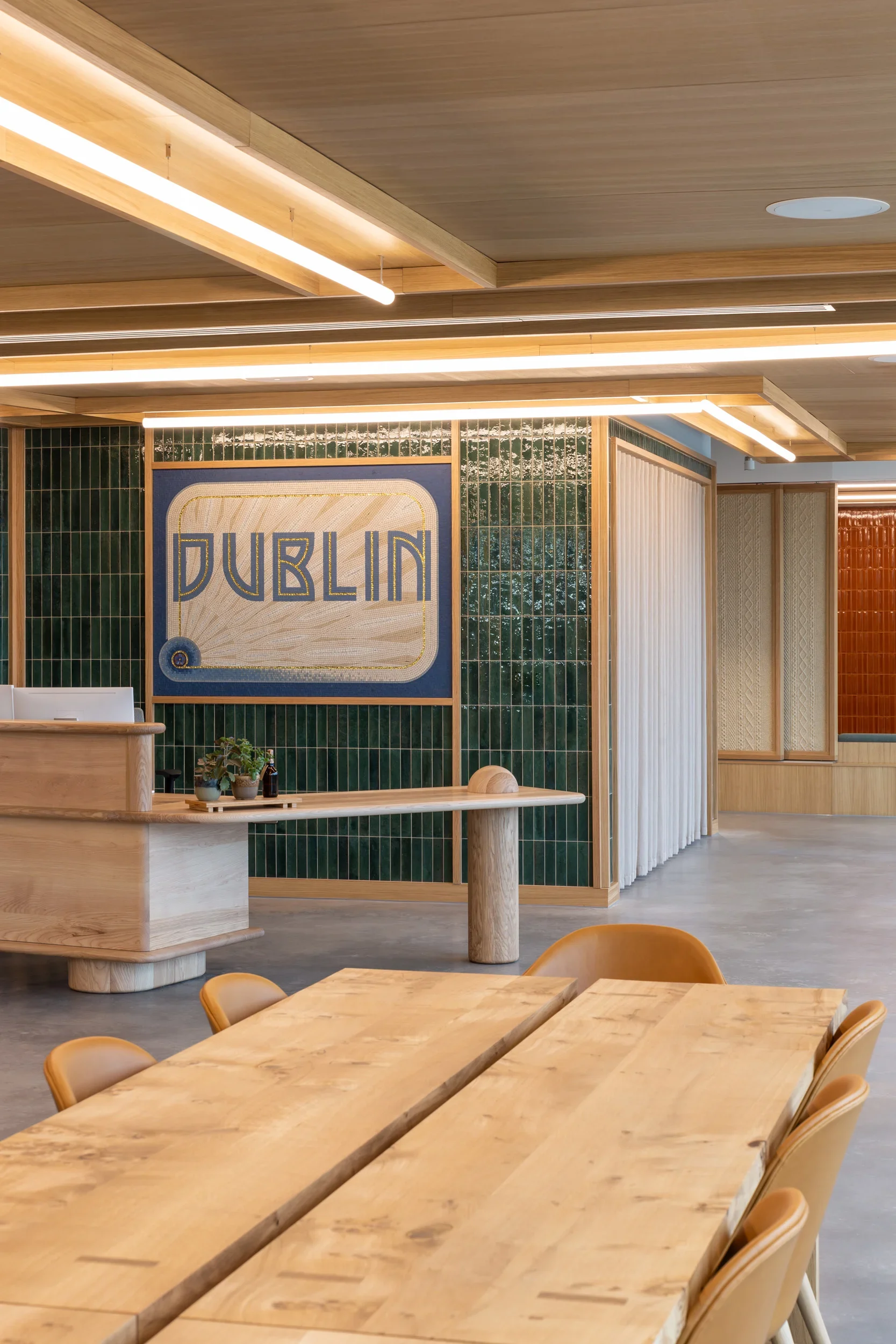 Interior of a modern restaurant or cafe with light wood furniture and ceiling, green tile walls, and a large sign that reads 'DUBLIN' with a decorative design.