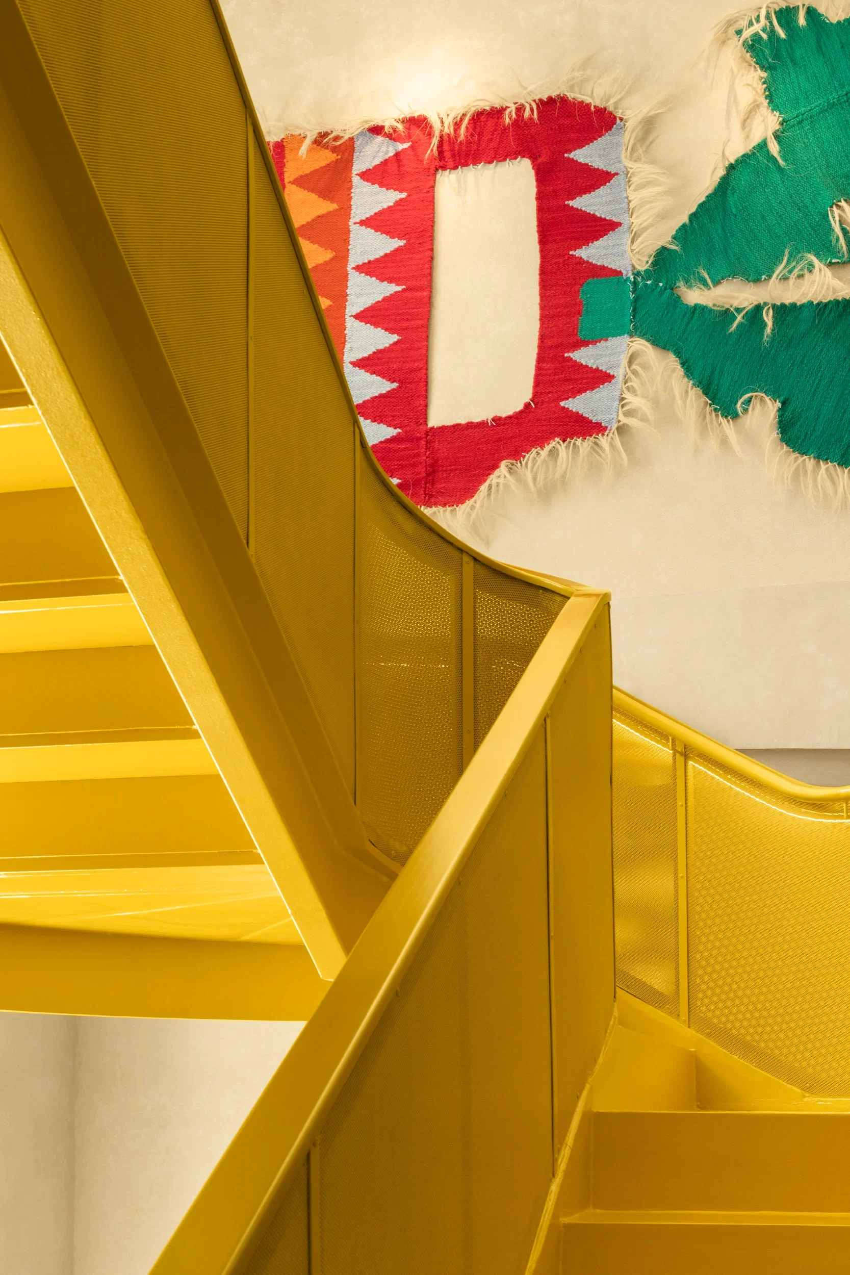 Yellow staircase with railings and a colorful rug on the floor with red, orange, blue, and white triangle patterns.
