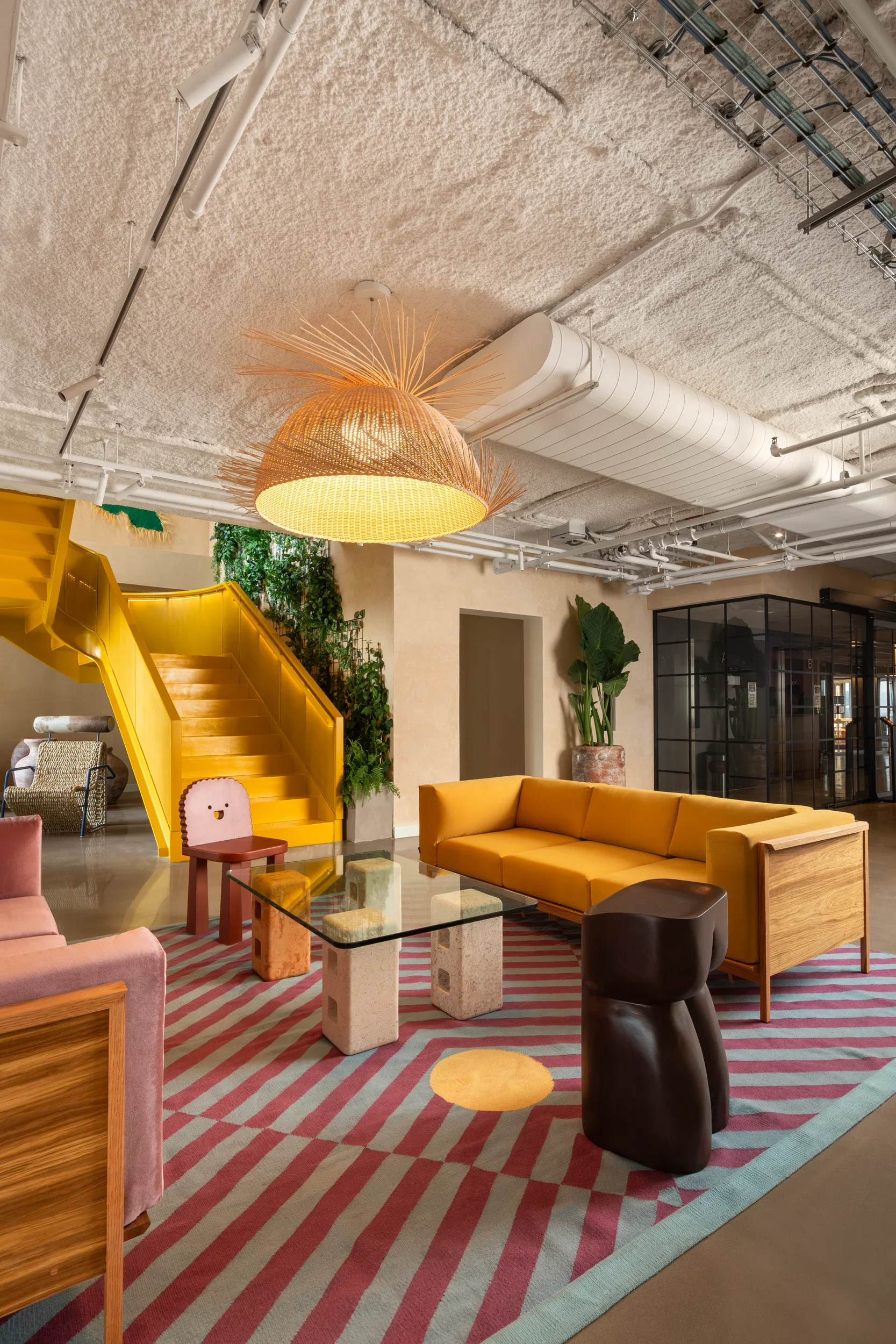 Colorful living room with yellow, pink, and black furniture, patterned rug, green plants, and modern decor.