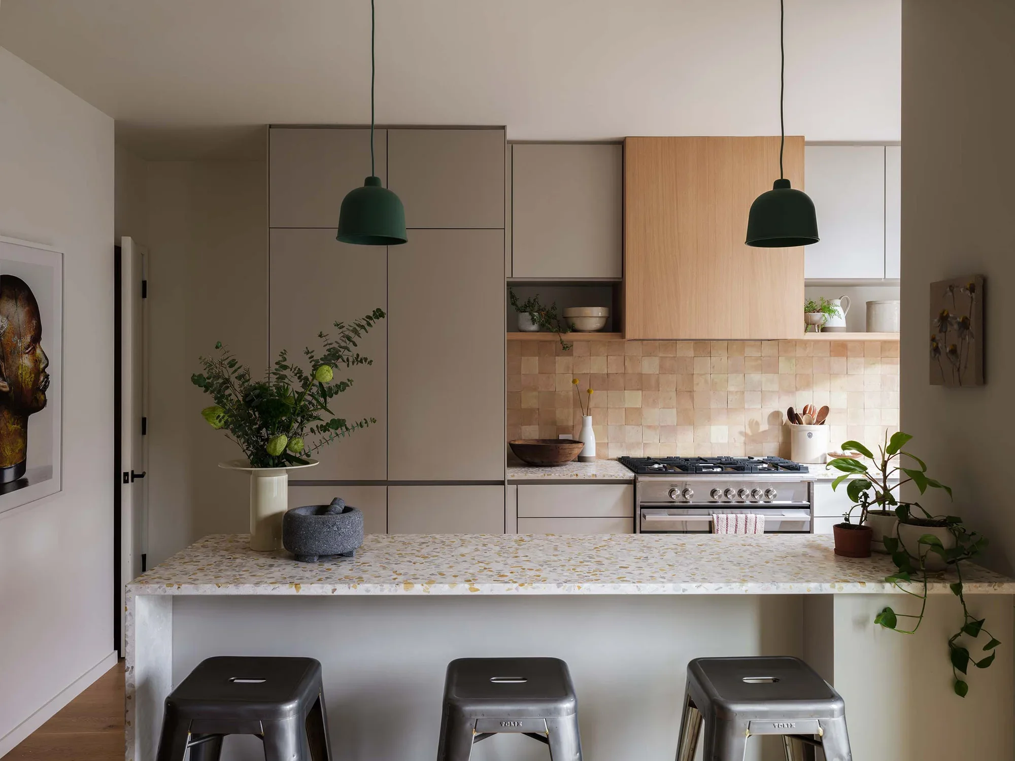 Modern kitchen with beige cabinets, a stove, plants, and pendant lighting.