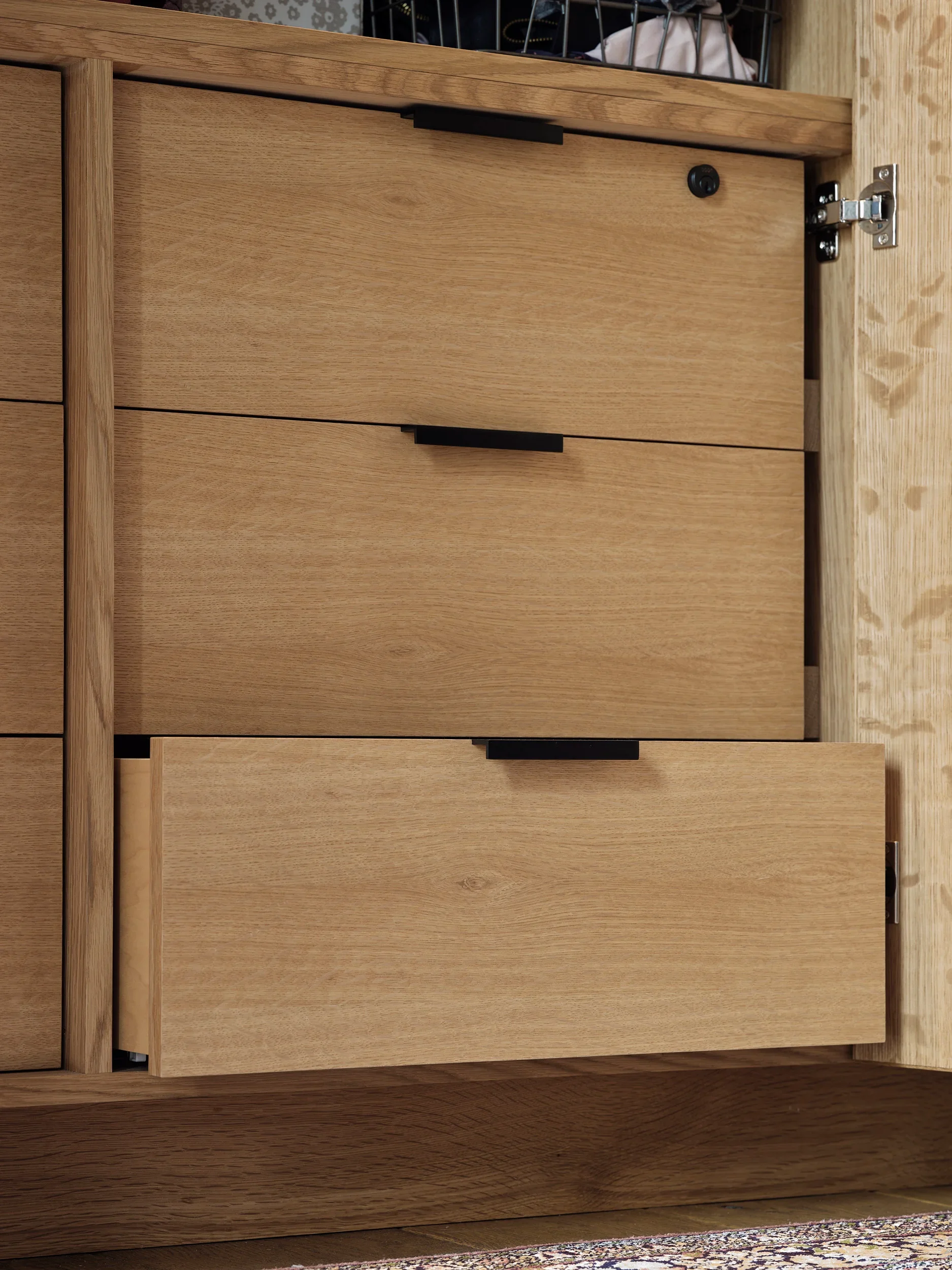 Close-up view of a wooden cabinet with metal hinges and handles, situated on a wooden surface with a patterned area rug beneath.
