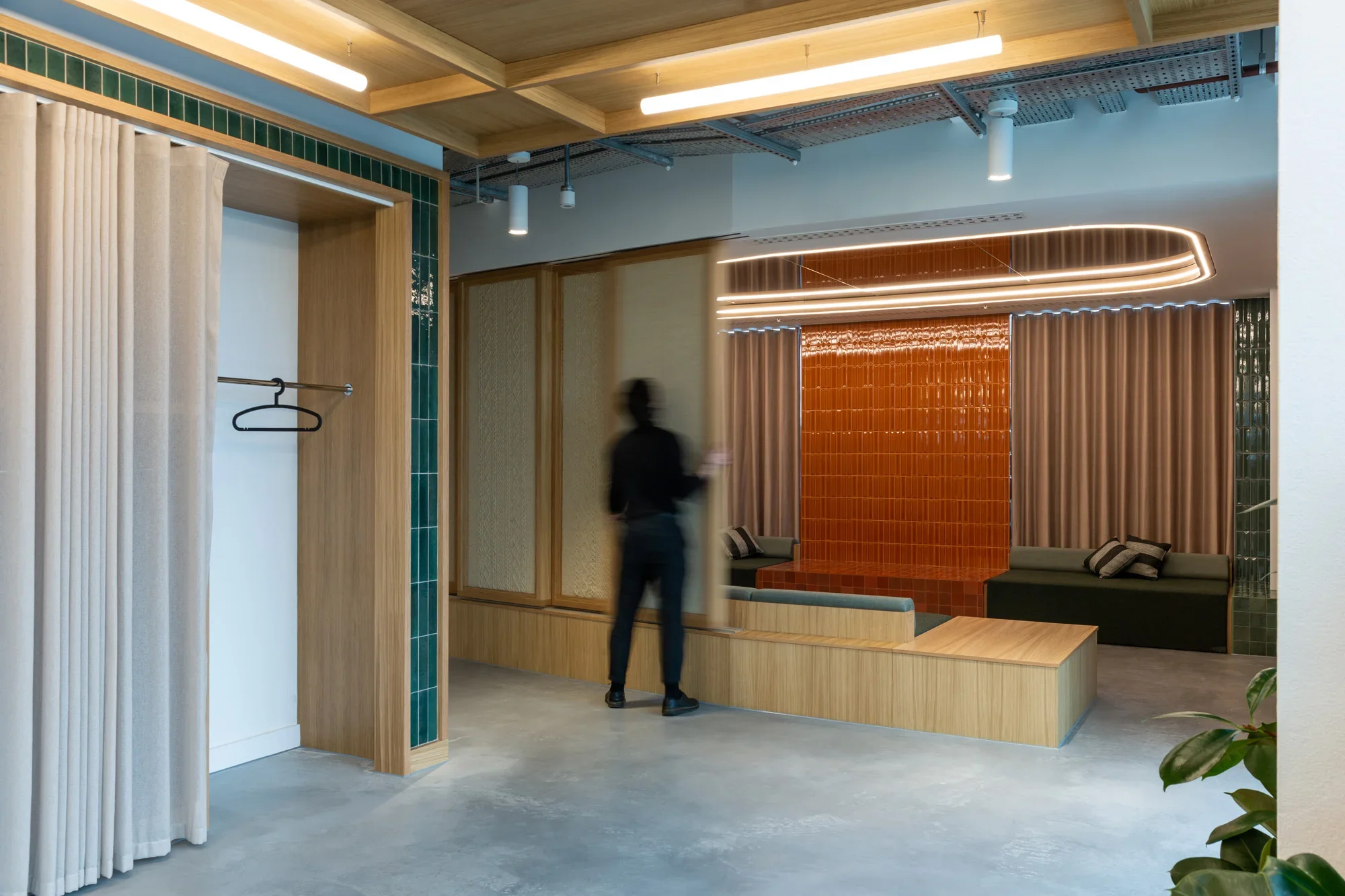 Modern interior with seating area featuring orange tiled wall, curtains, and a person walking through.