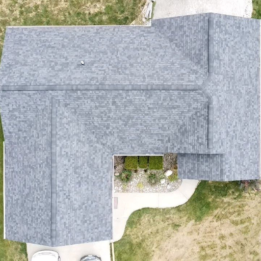 Aerial view of a house with a grey shingle roof, surrounding lawn, and a small garden area near the entrance.