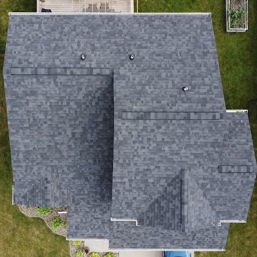 An aerial view of a house with a gray shingled roof and surrounding green lawn. The roof has three vents and features multiple slopes and sections.