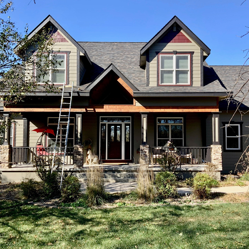 Front view of a two-story house with a porch, sliding glass doors, and dormer windows, surrounded by a landscaped yard with grass and plants.