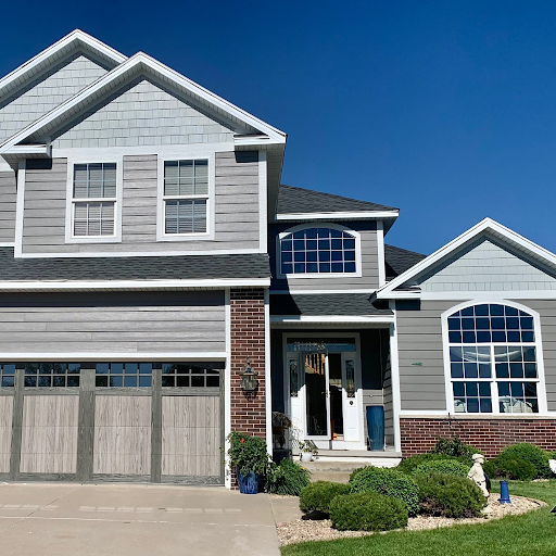 A two-story house with gray siding, brick accents, and a two-car garage under a clear blue sky.