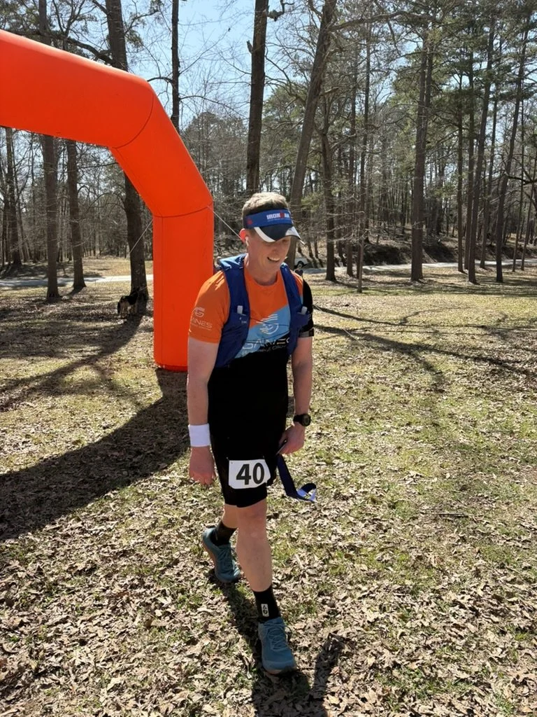 Young man wearing a race bib number 40, sporting out-fit for a running event, walking on a trail in a forest with leafless trees, under a clear sky.