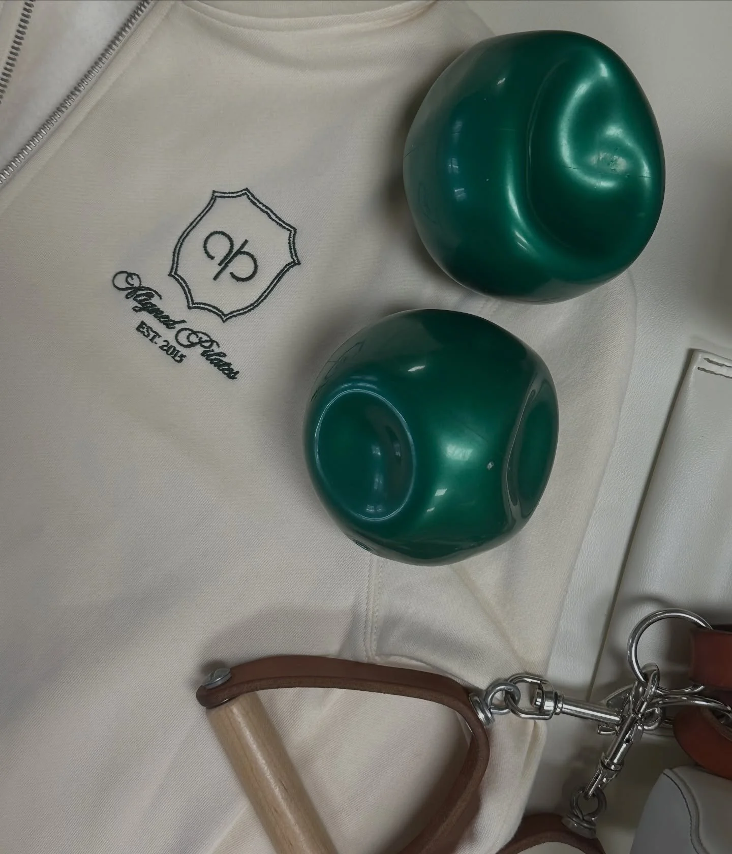 Two green pilates balls on top of a white sweatshirt with green embroidery of the Aligned Pilates logo.