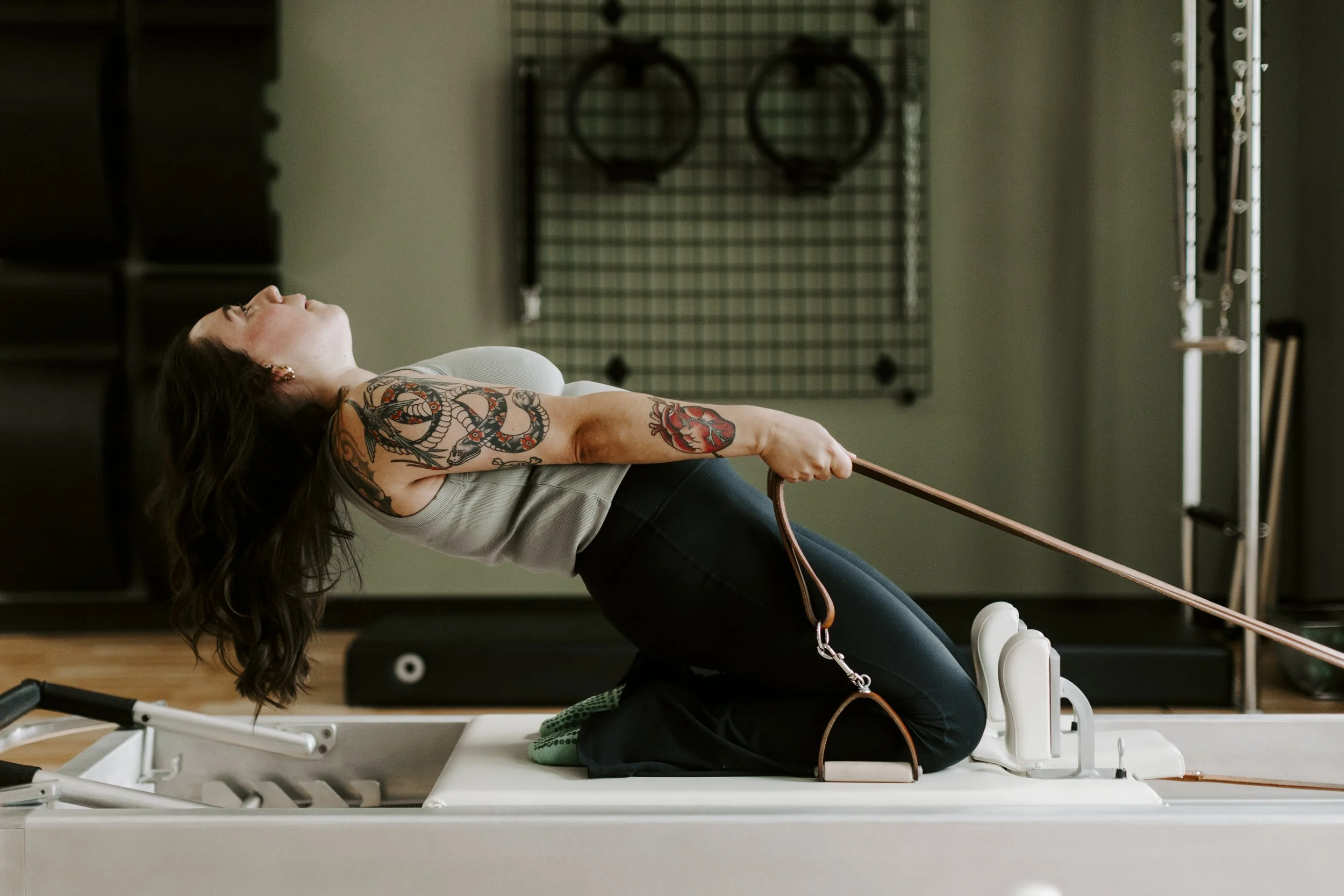 Woman with tattoos practicing Pilates on a reformer machine in a gym.