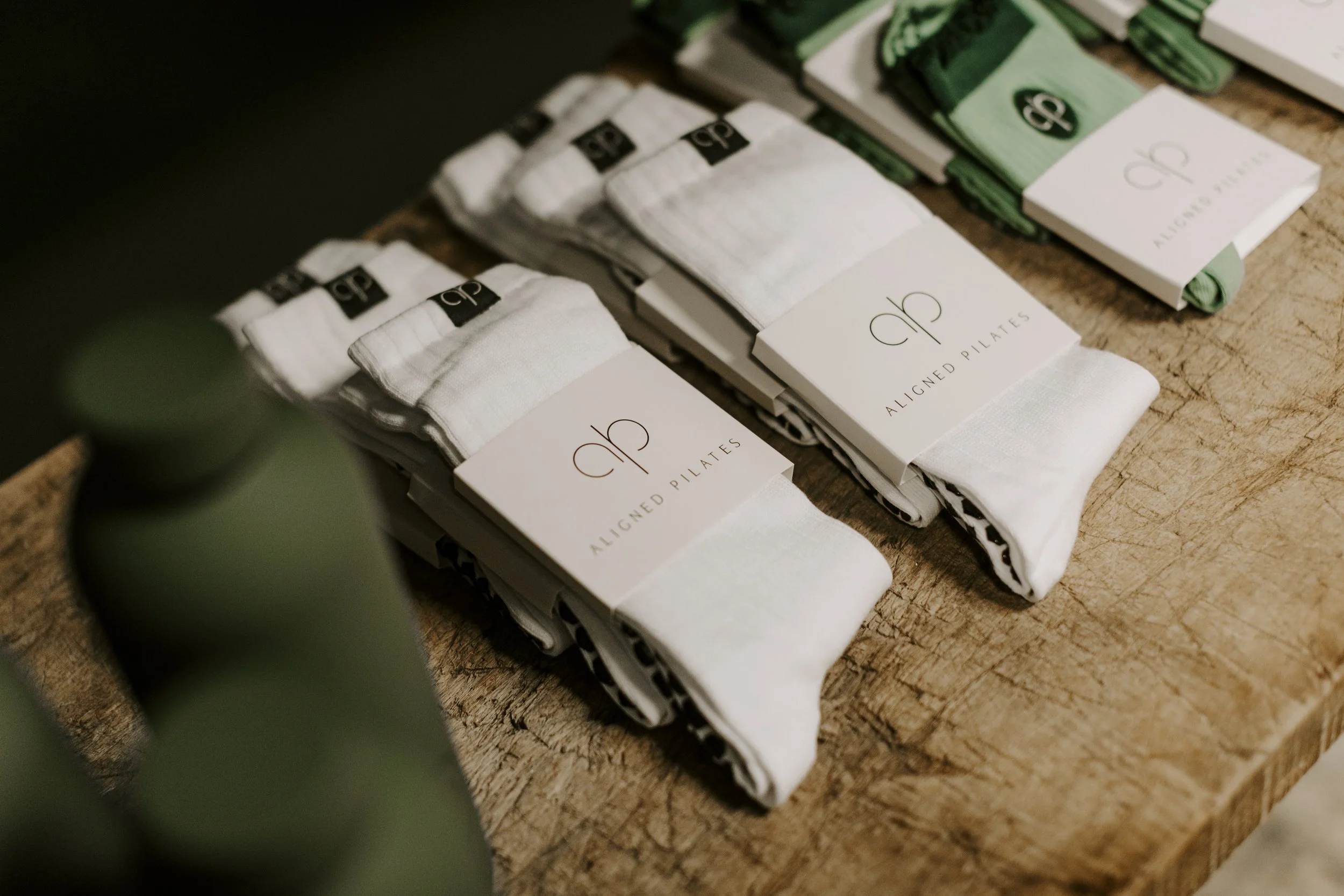 Stacked socks with black and white or green and white packaging labeled 'Aligned Pilates' on a wooden surface.