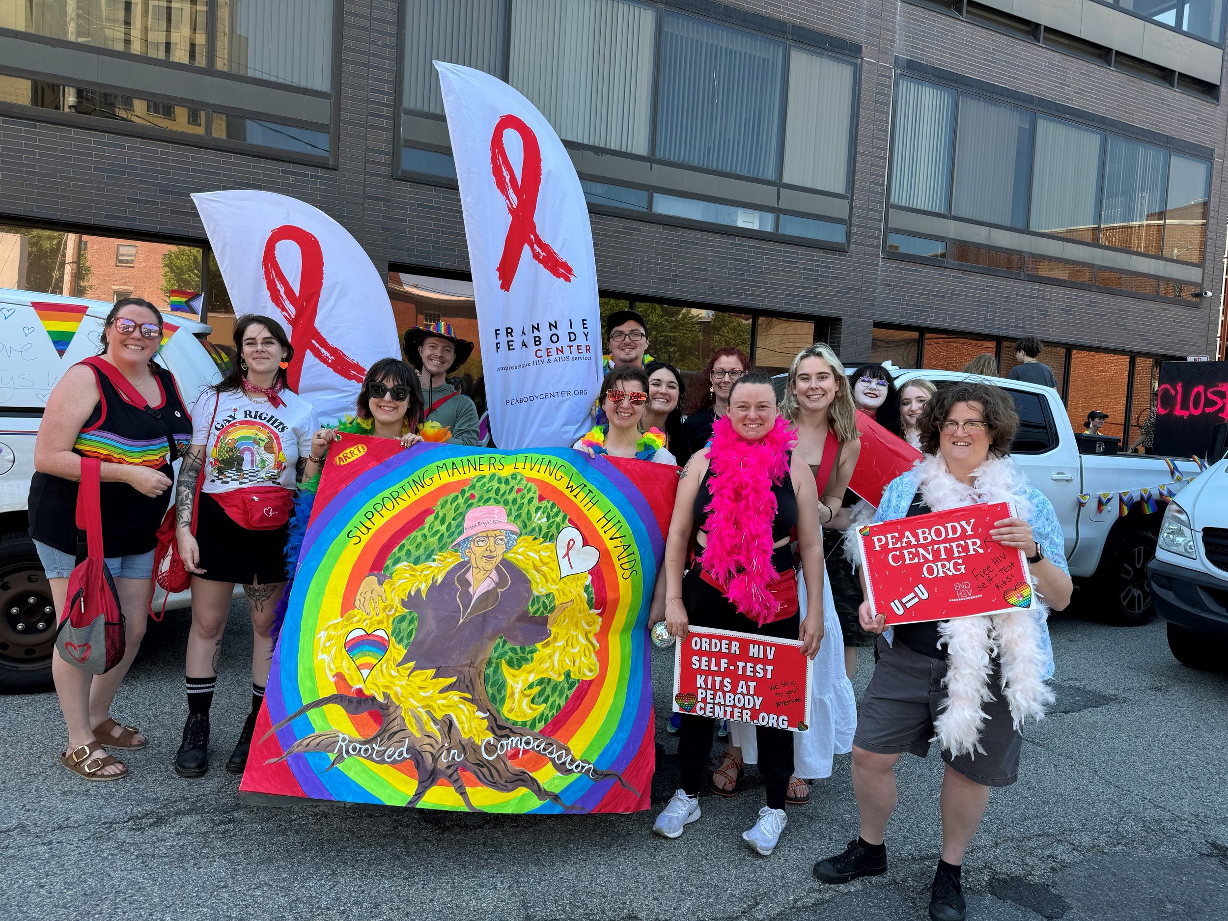 A diverse group of people participating in a pride parade holding rainbow flags and a colorful banner.